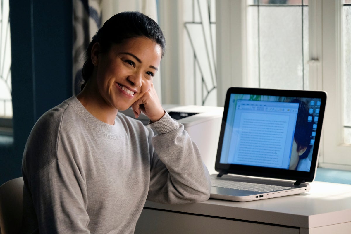 Gina Rodriguez sits next to a laptop, smiling.