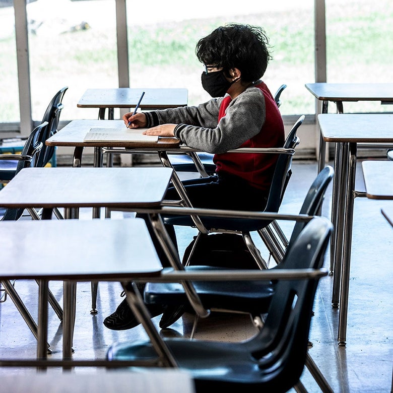 A student in a mask sits at a desk along in a classroom.