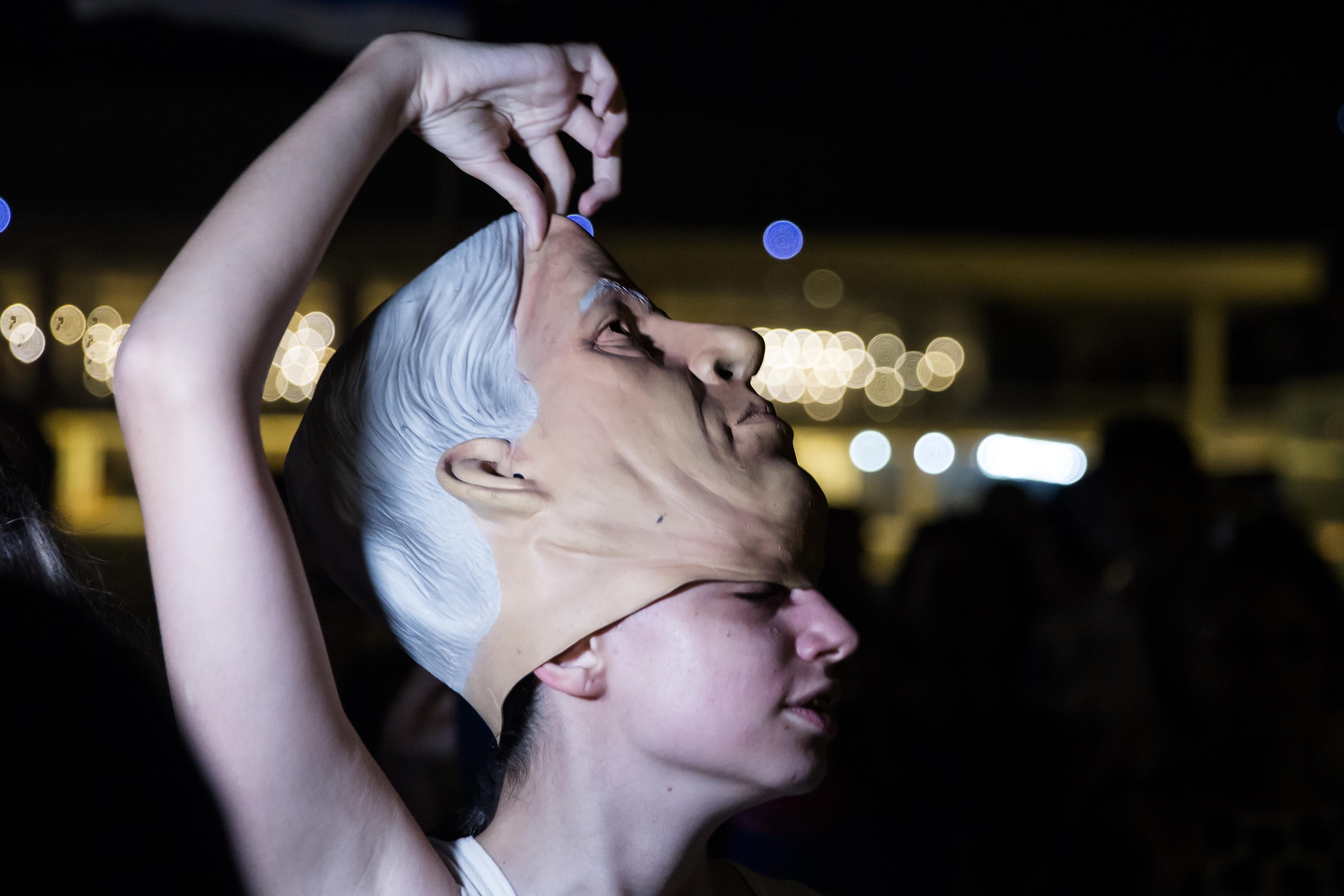 A young woman pulls a mask of Benjamin Netanyahu's face off her head