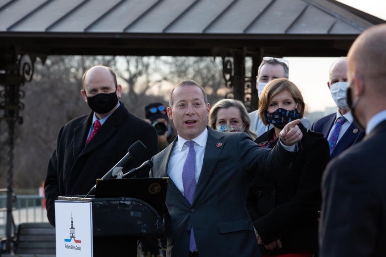 Gottheimer points with his left hand as he speaks at a podium with representatives standing around him