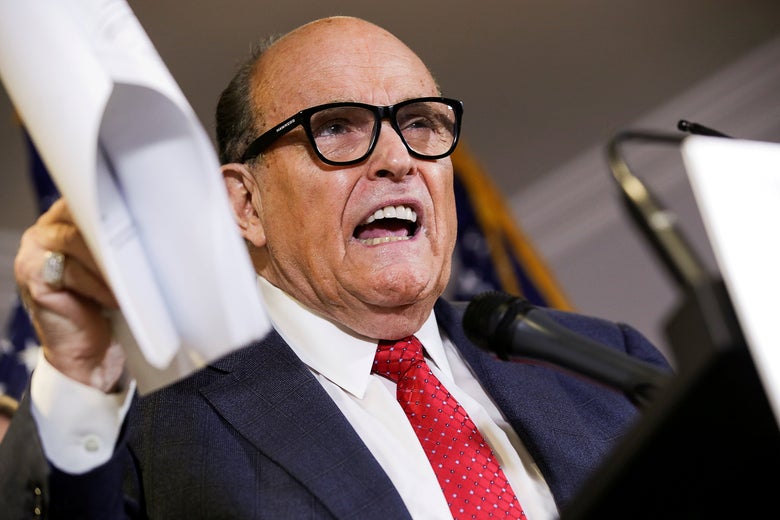 Giuliani speaks at a podium while holding up a packet of papers in one hand
