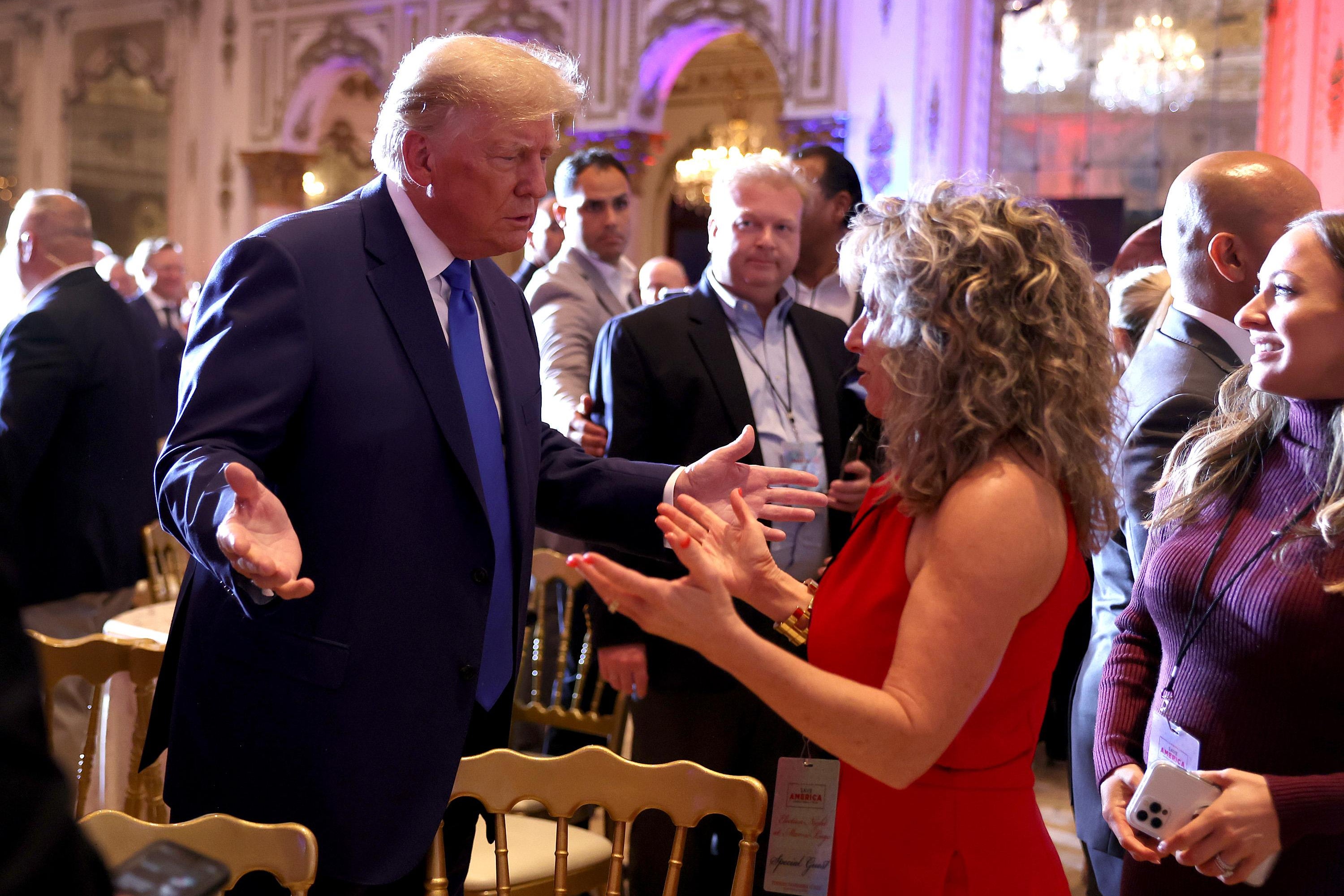 Former U.S. President Donald Trump mingles with supporters during an election night event at Mar-a-Lago. He's shrugging his shoulders at the woman he's talking to.
