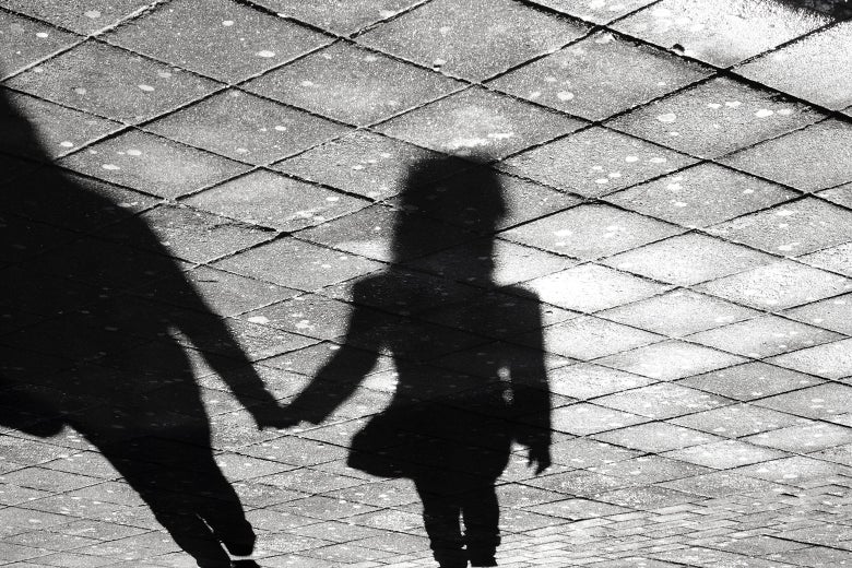 Shadows of a mother holding her daughter's hand are cast onto a stone path.