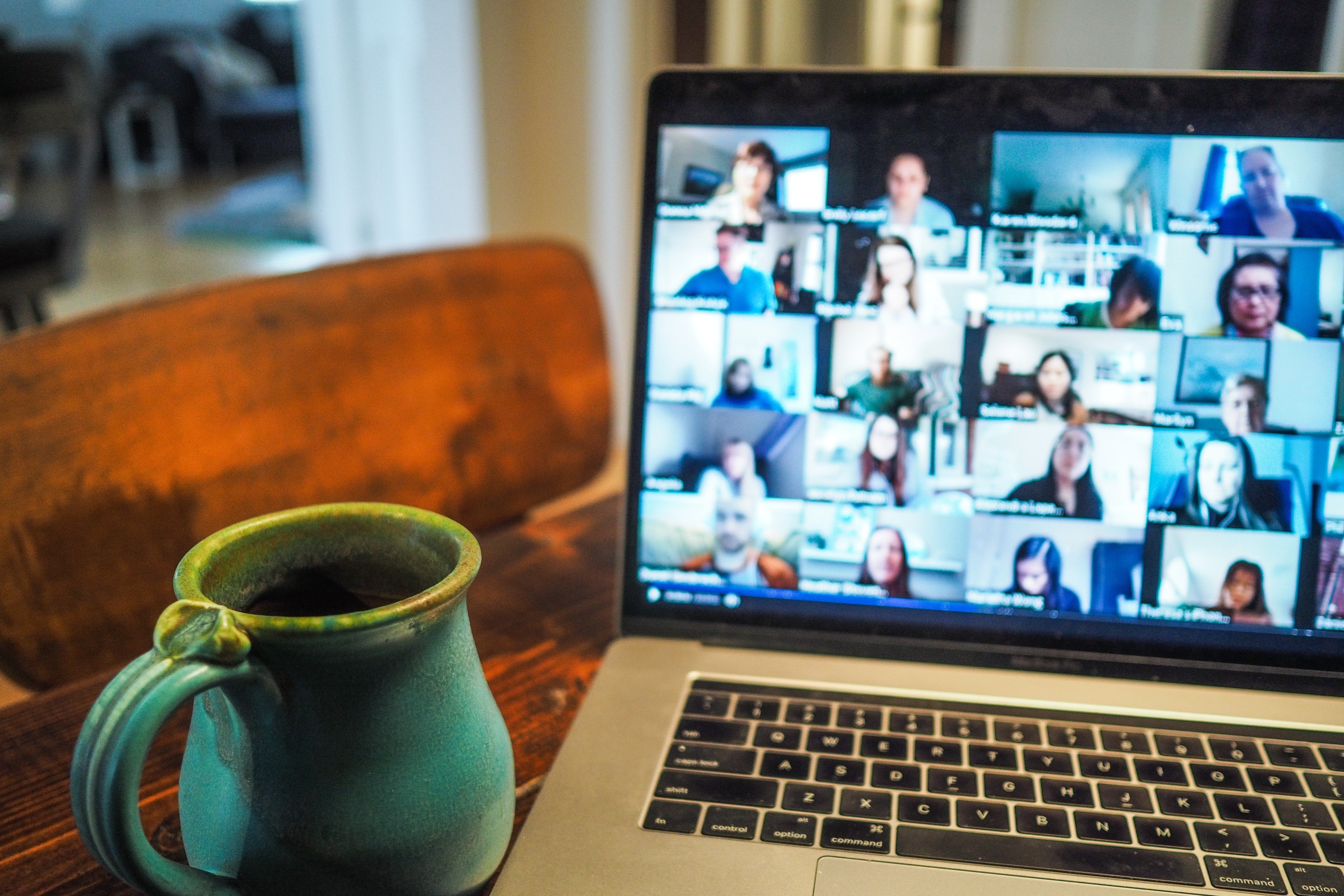 A mug and laptop showing a grid of faces on Zoom sit on a table.