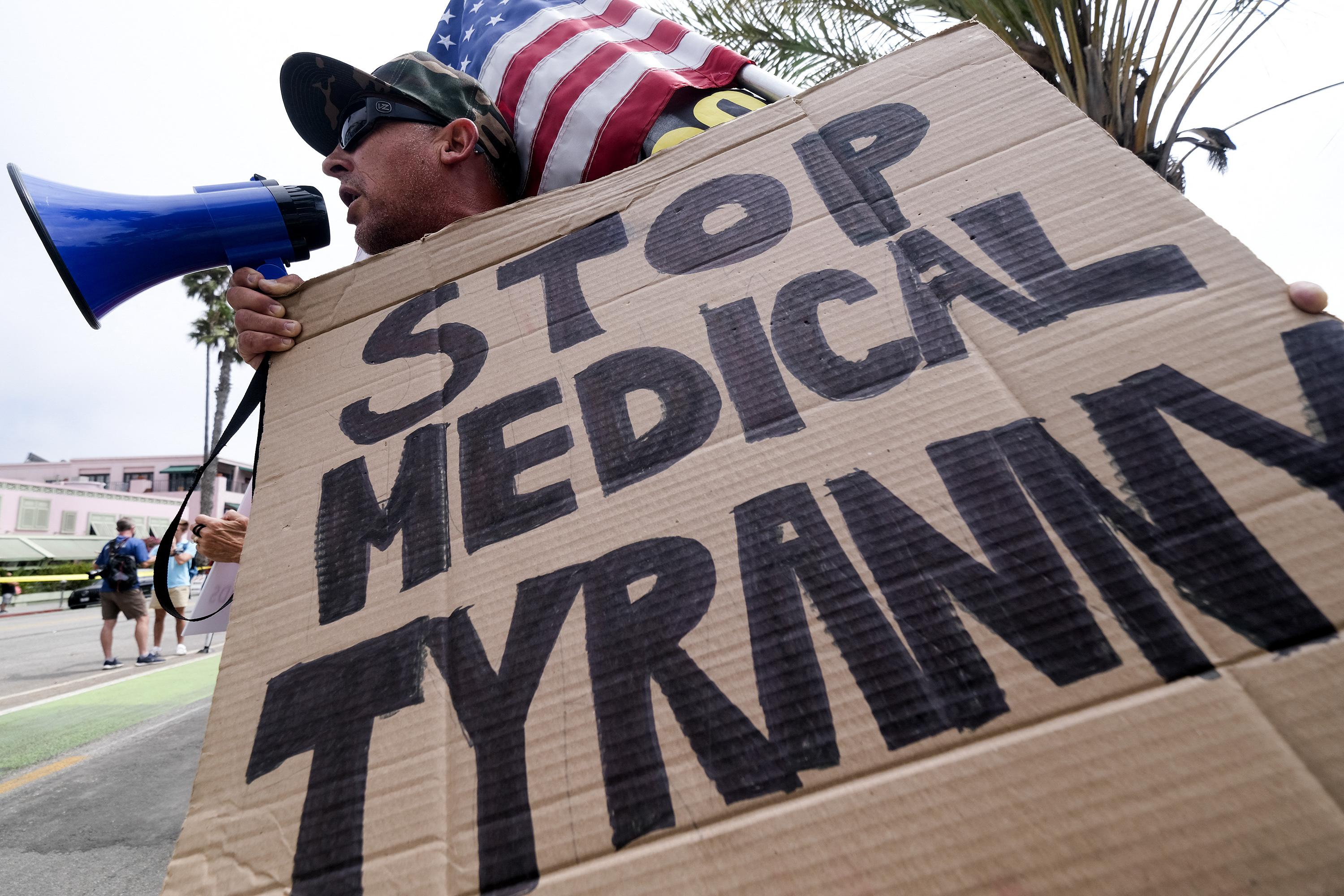An anti-vaccination protester uses a bullhorn and holds a sign that says STOP MEDICAL TYRANNY and an American flag as he takes part in a rally against COVID-19 vaccine mandates.