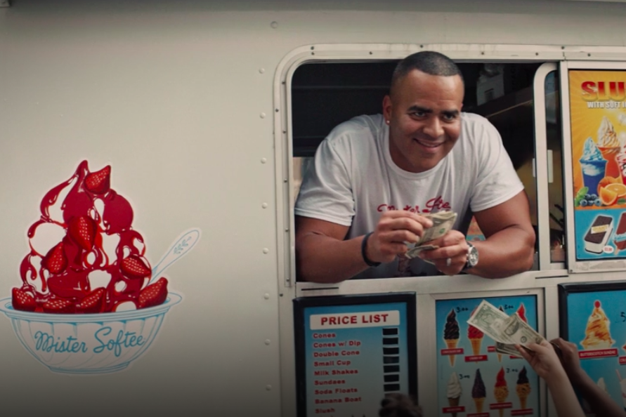 Chris Jackson leans out the window of an ice cream truck, smirking and holding a stack of dollar bills.