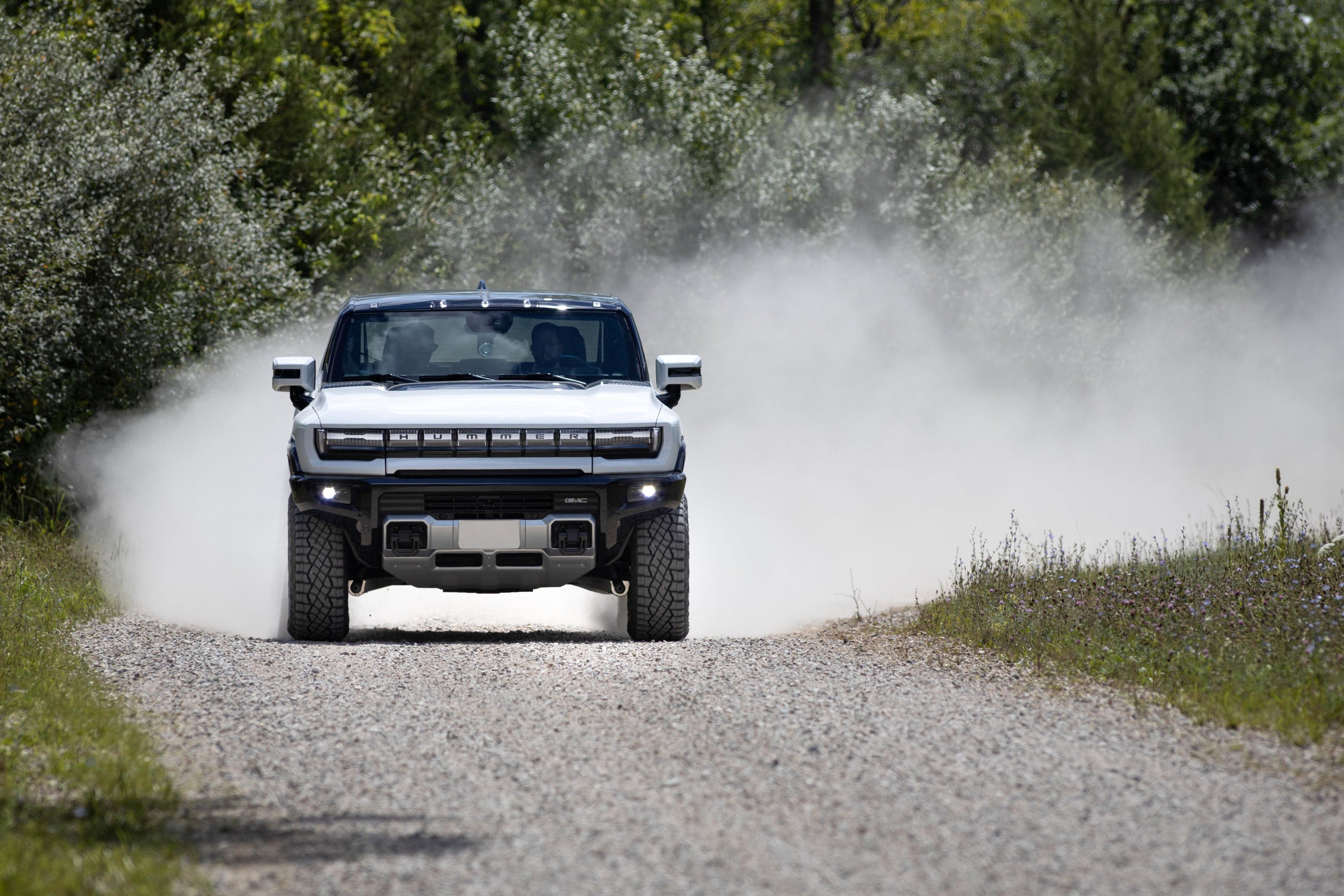 A silver Hummer EV drives down a dusty road.