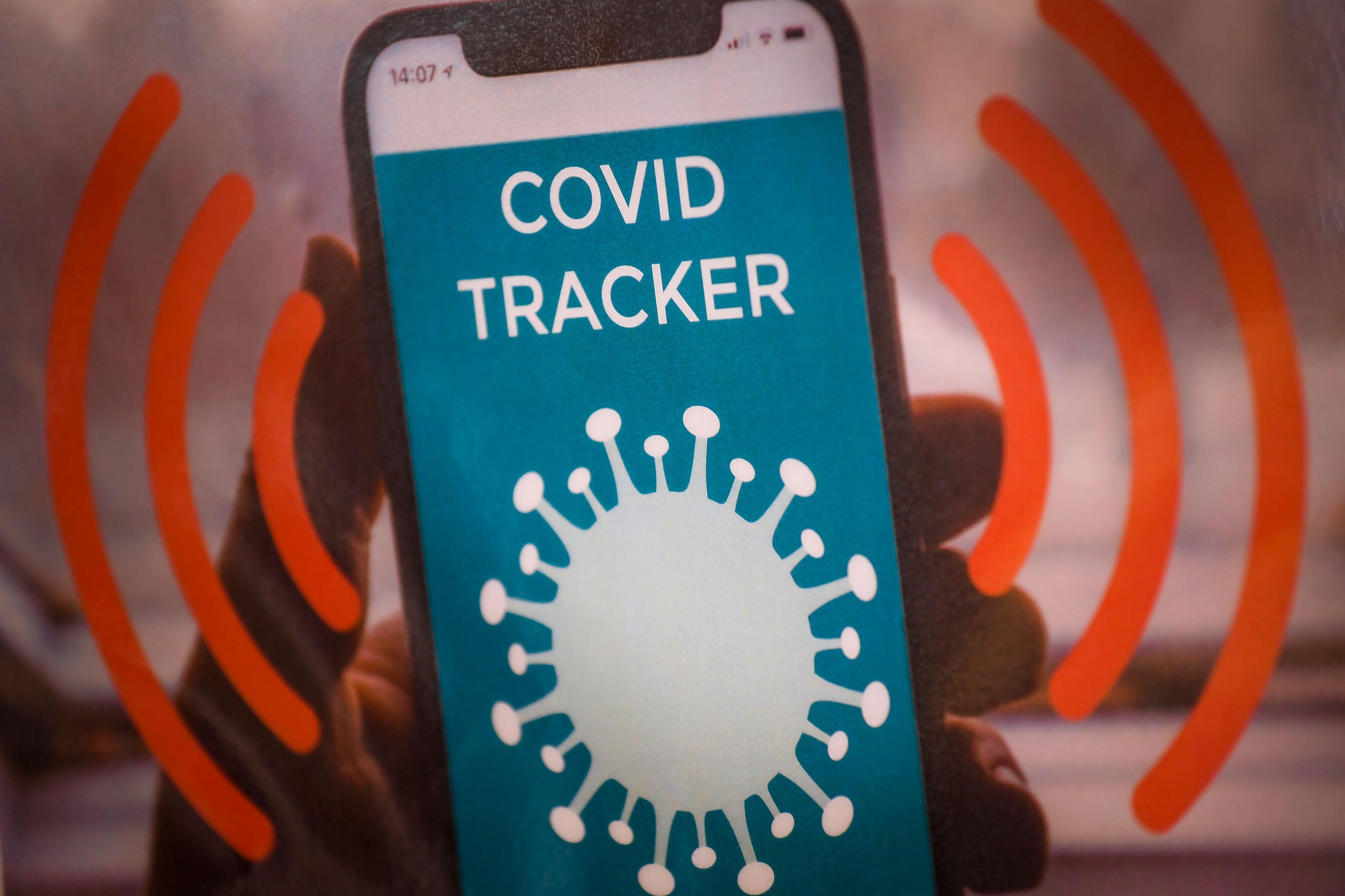 An iPhone with the words "COVID TRACKER" is held in a hand, with red stylized waves coming off the phone.