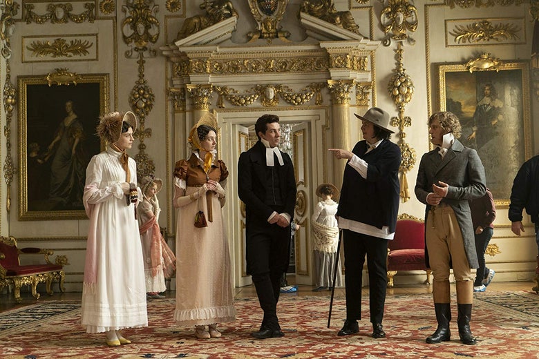 Director Autumn de Wilde points as Amber Anderson, Tanya Reynolds, Josh O'Connor, and Johnny Flynn, all wearing Regency-era clothing, look on. They're standing in an ornate room decorated with paintings and a fancy rug.