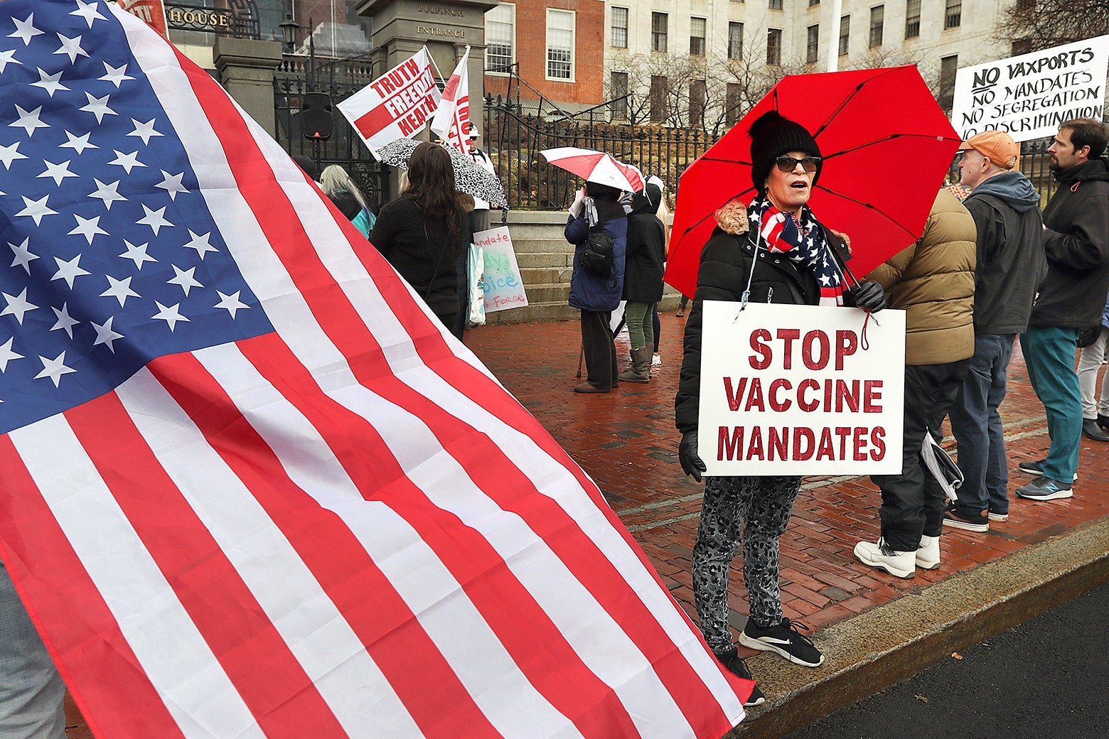 A protester wears a sign that reads, "Stop vaccine mandates" next to a person wearing an American flag. 