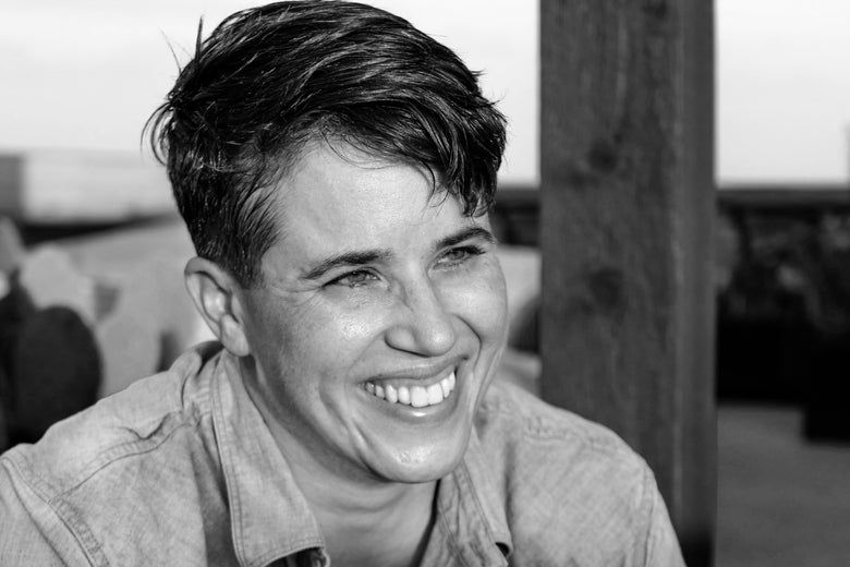 Black and white photo of a woman with short hair smiling broadly next to a wooden post