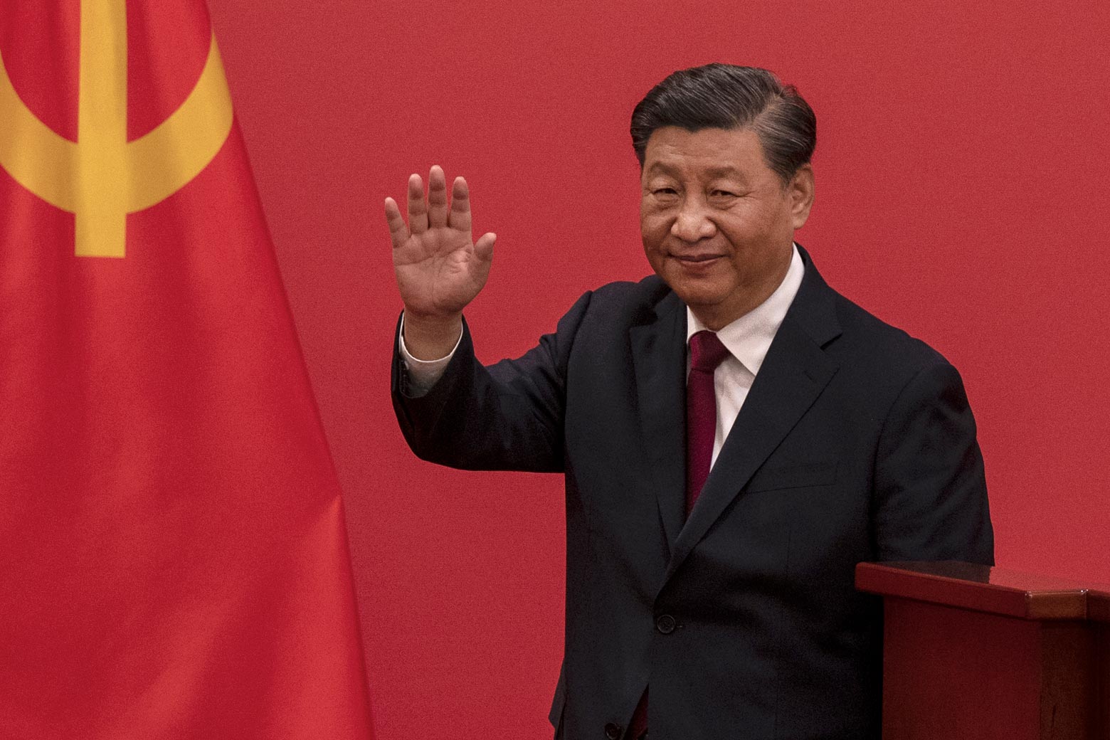 Chinese President Xi Jinping waves from in front of the red background of the Chinese flag.