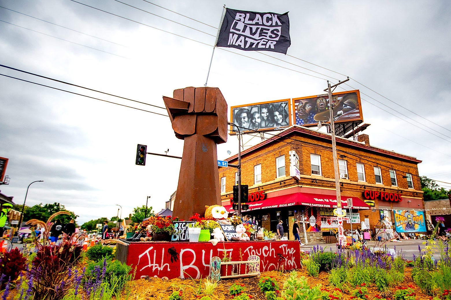 A wooden raised fist statue stands in the middle of an intersection that has become a memorial.