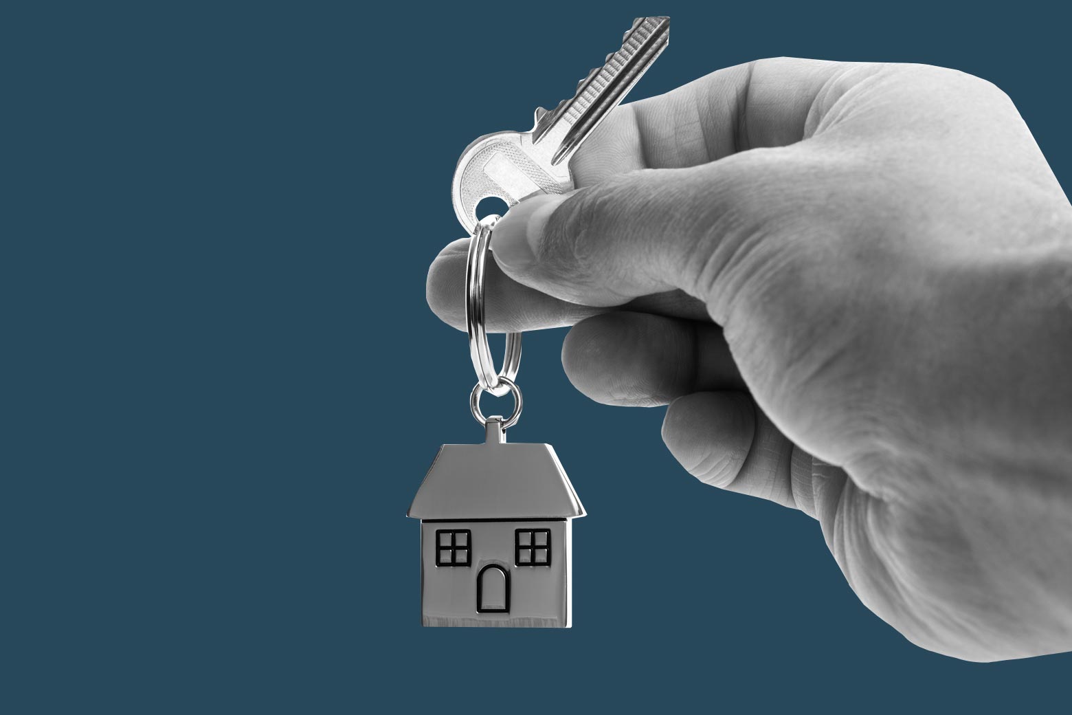 A hand holds a key that includes a keychain shaped like a house.