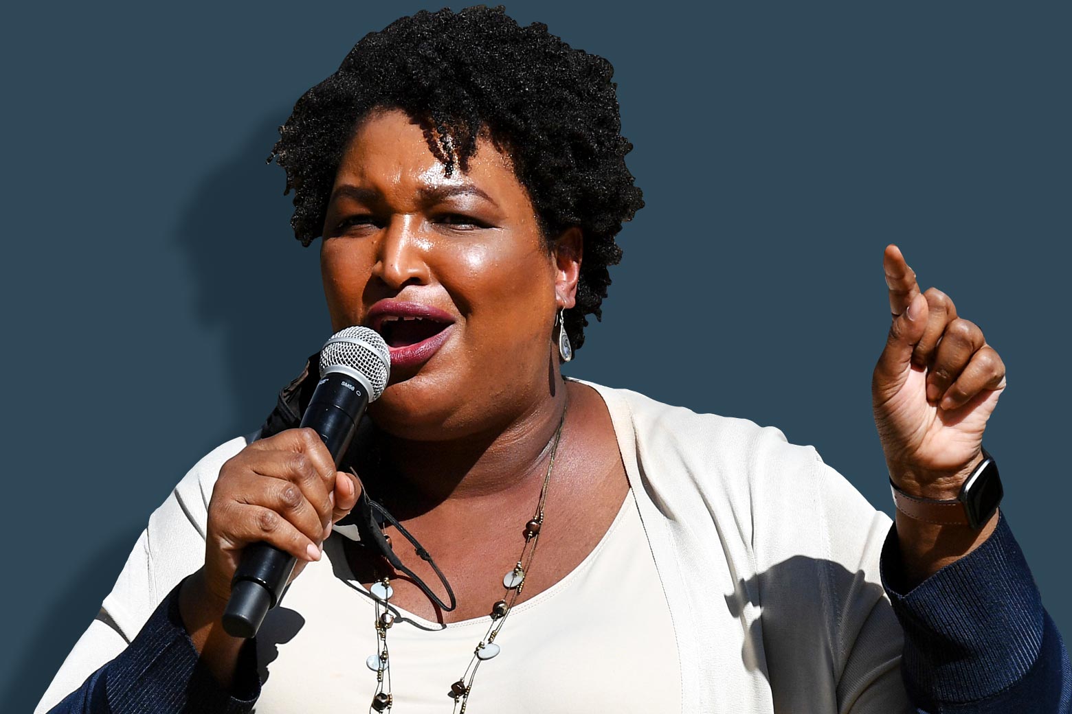 Stacey Abrams speaks, holding a mic in one hand and pointing with the other hand