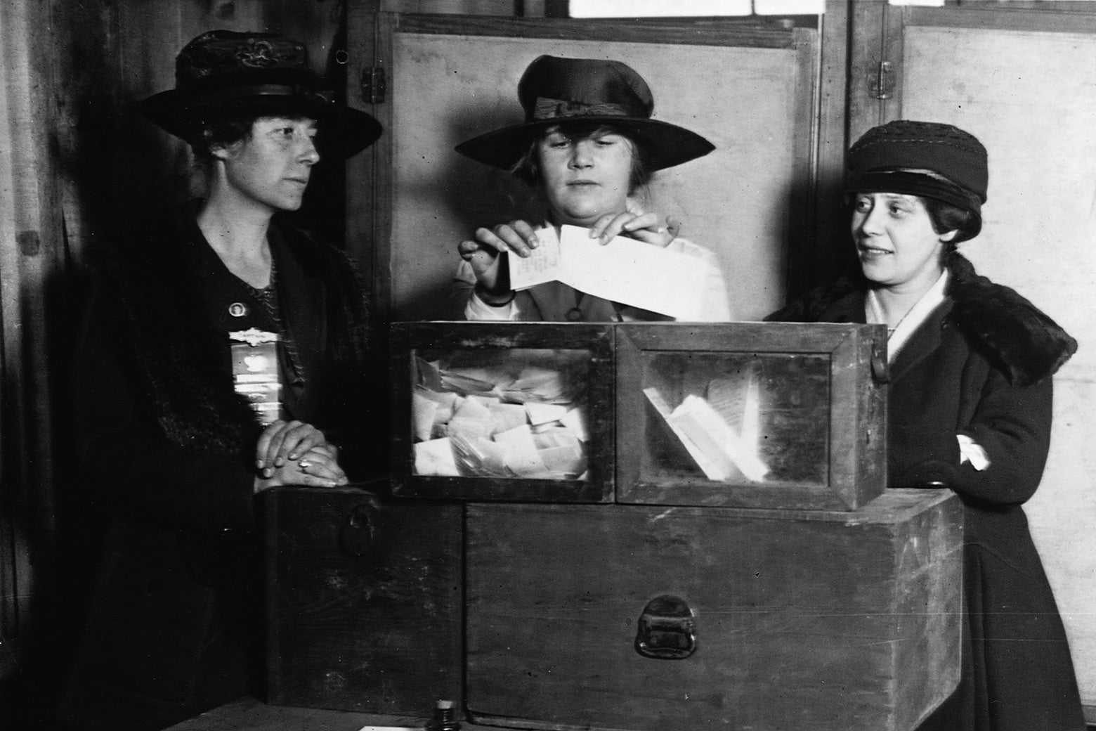A woman places a ballot in a box as two women on either side of her watch