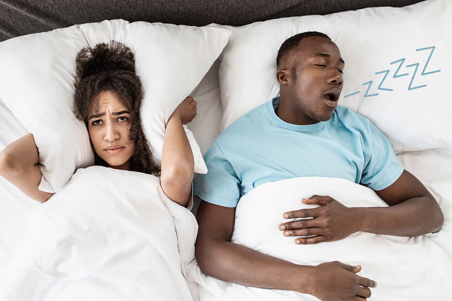 A couple in a bed with the man snoring and Zzz coming out of his mouth and a woman with insomnia holding a pillow over her ears. 