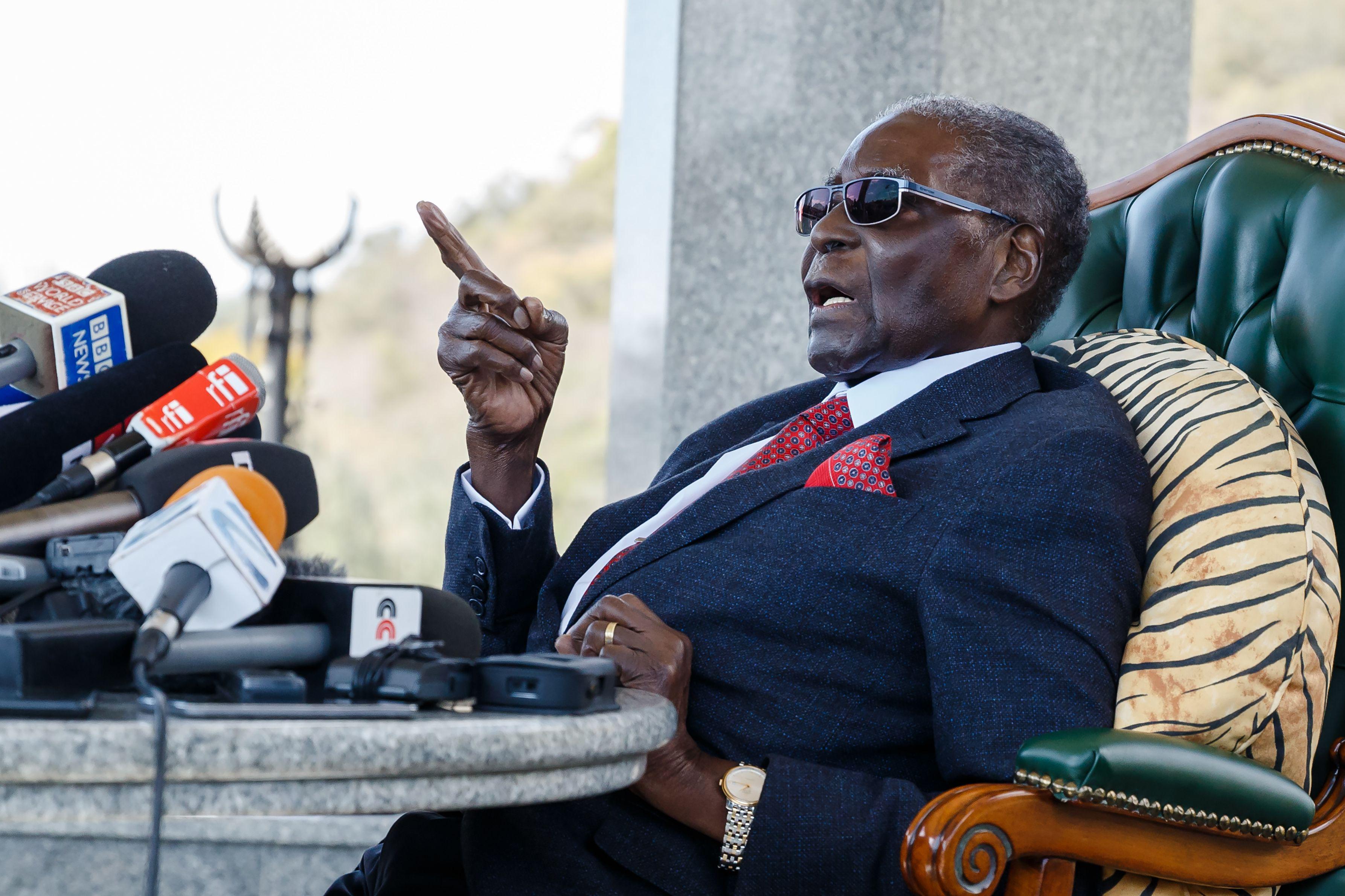 Mugabe slouched back in a chair wearing sunglasses and speaking into a microphone