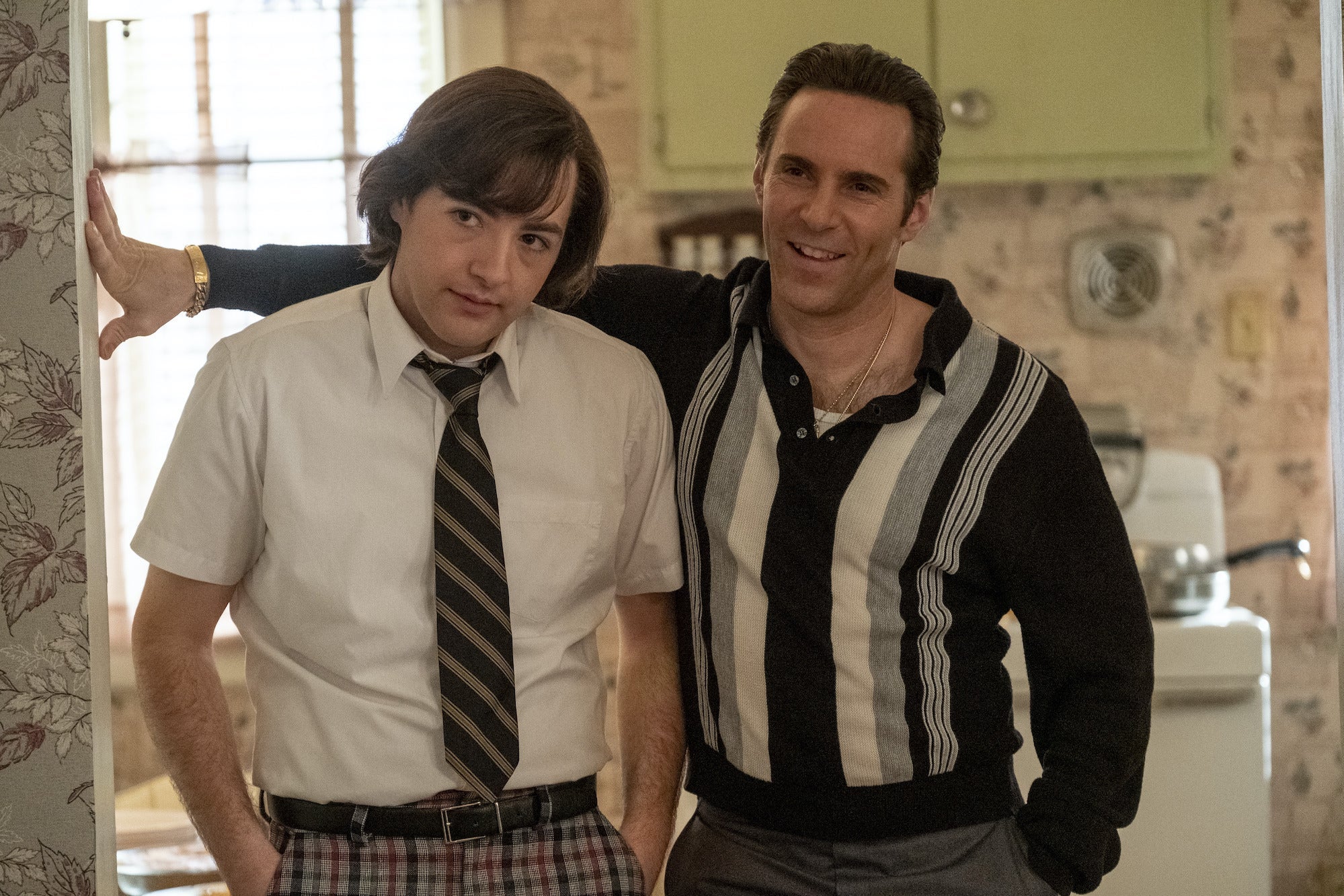 Michael Gandolfini as young Tony standing with stooped shoulders in a kitchen with Alessandro Nivola as Tony's uncle Dickie smiling and leaning over him