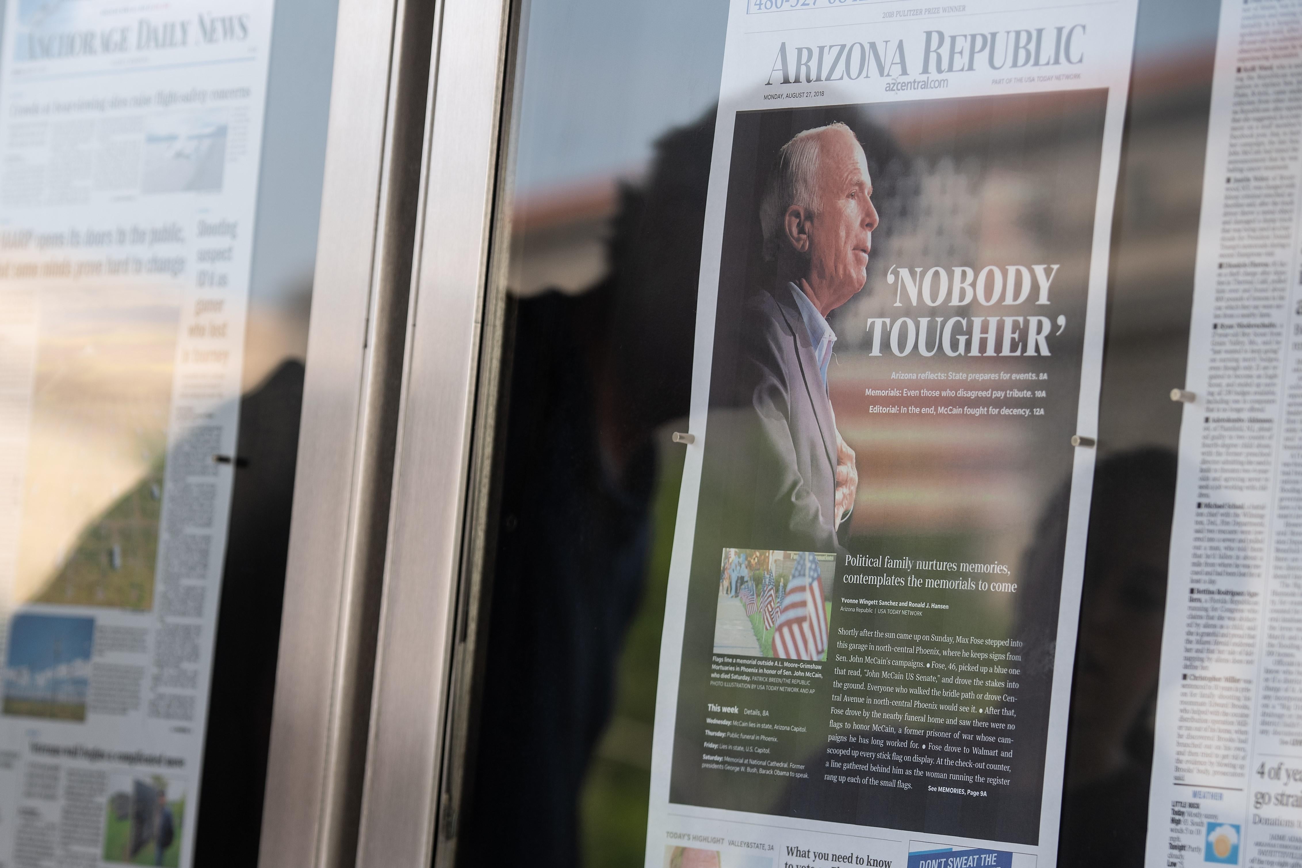 A reflection of people looking at the front page of the Arizona Republic with a picture of John McCain