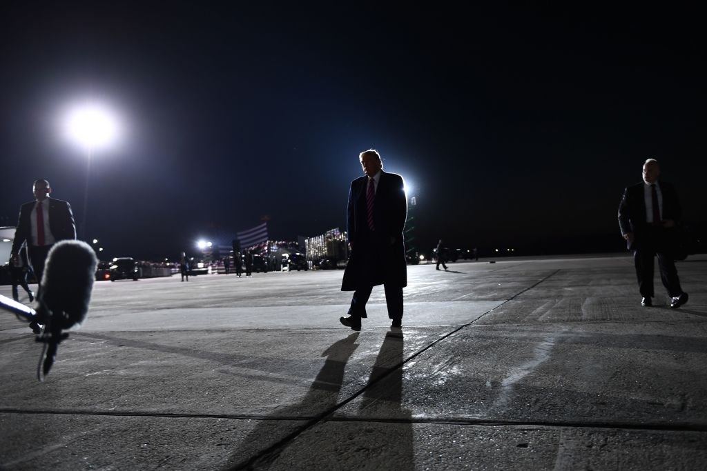 Trump, wearing a long coat, walks across an airport tarmac.