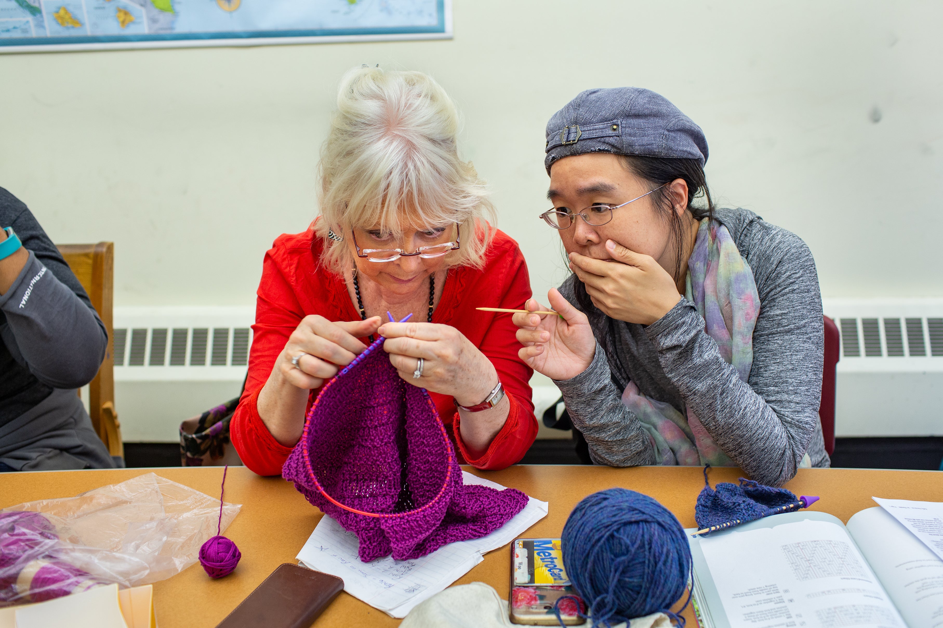 A woman helps another woman with her knitting.