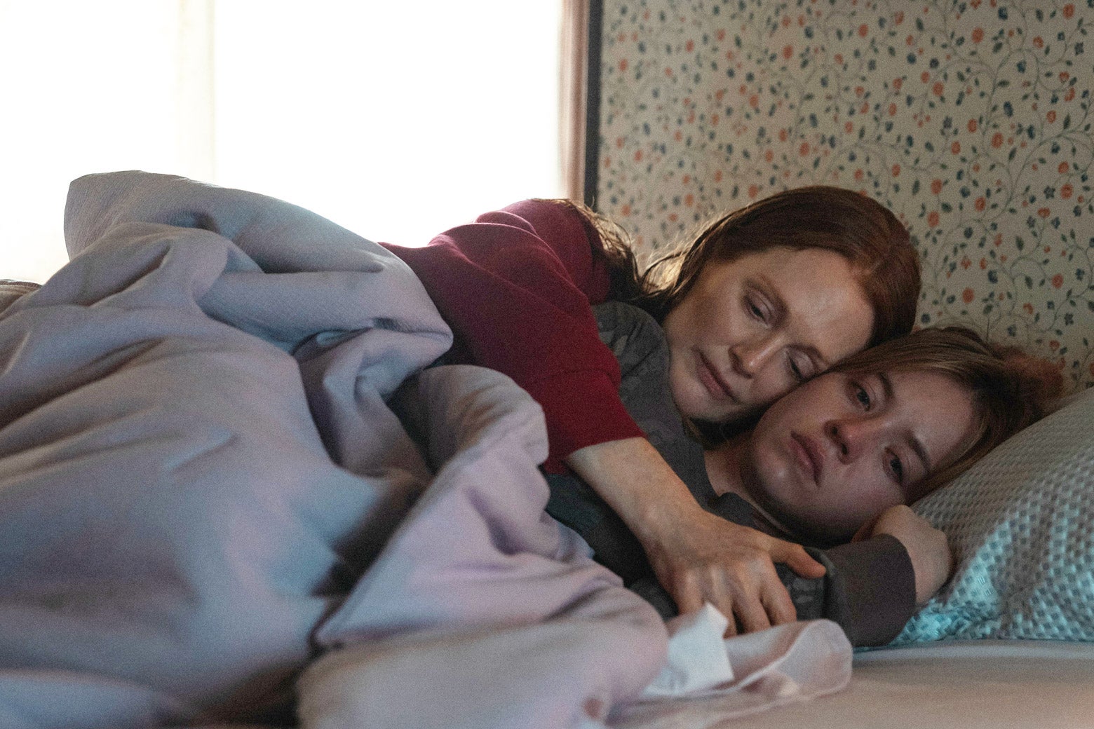 The mom and daughter characters are lying on a bed hugging and looking sad.