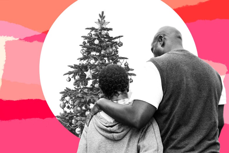 A man puts his arm around his son as they stand in front of a Christmas tree.