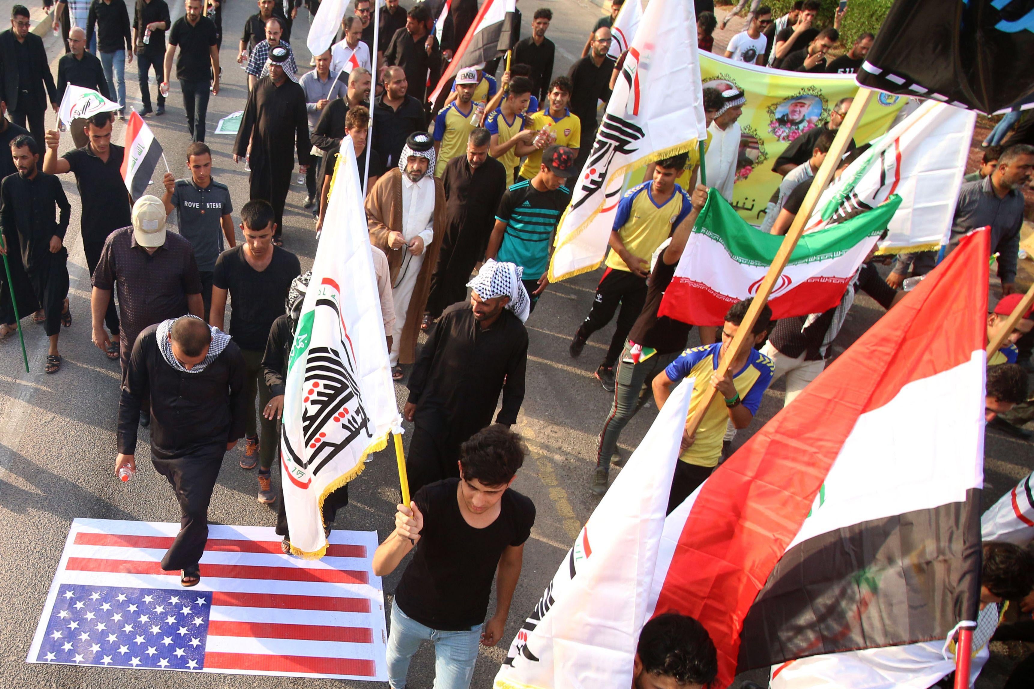 Demonstrators waving Iranian and pro-Iranian party flags step on a U.S. flag as they march