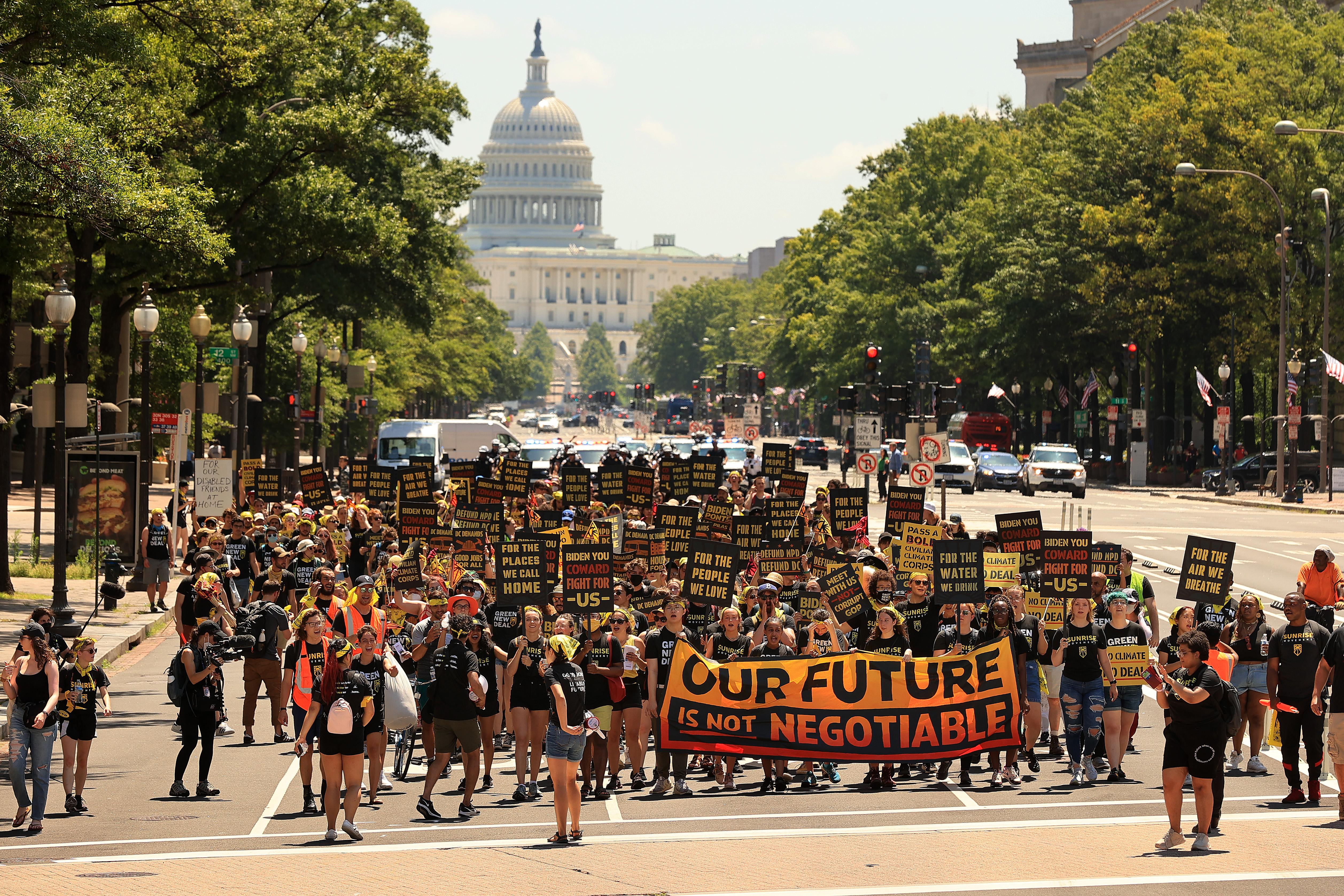 Hundreds of young climate activists marching along Pennsylvania Avenue to the White House. The Capitol is behind them, and they carry a sign with the phrase "Our future is not negotiable."