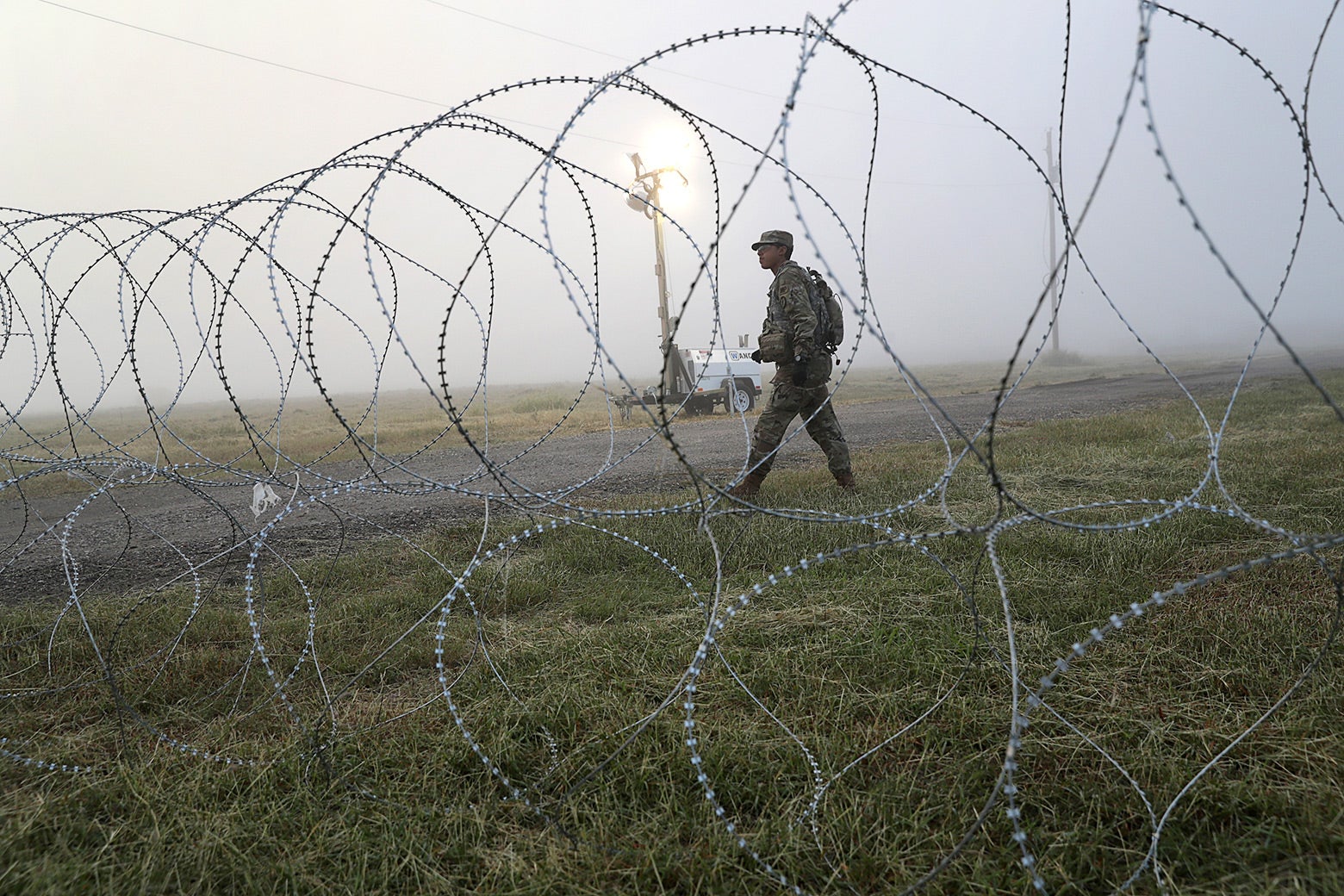 A soldier walking beside a barbed wire fence.