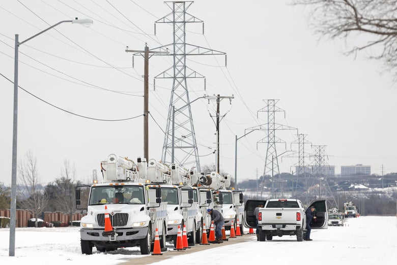 A line of trucks carrying electrical equipment are parked in the snow under power lines.