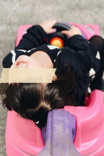 A little girl with a strip of cardboard over her eyes.