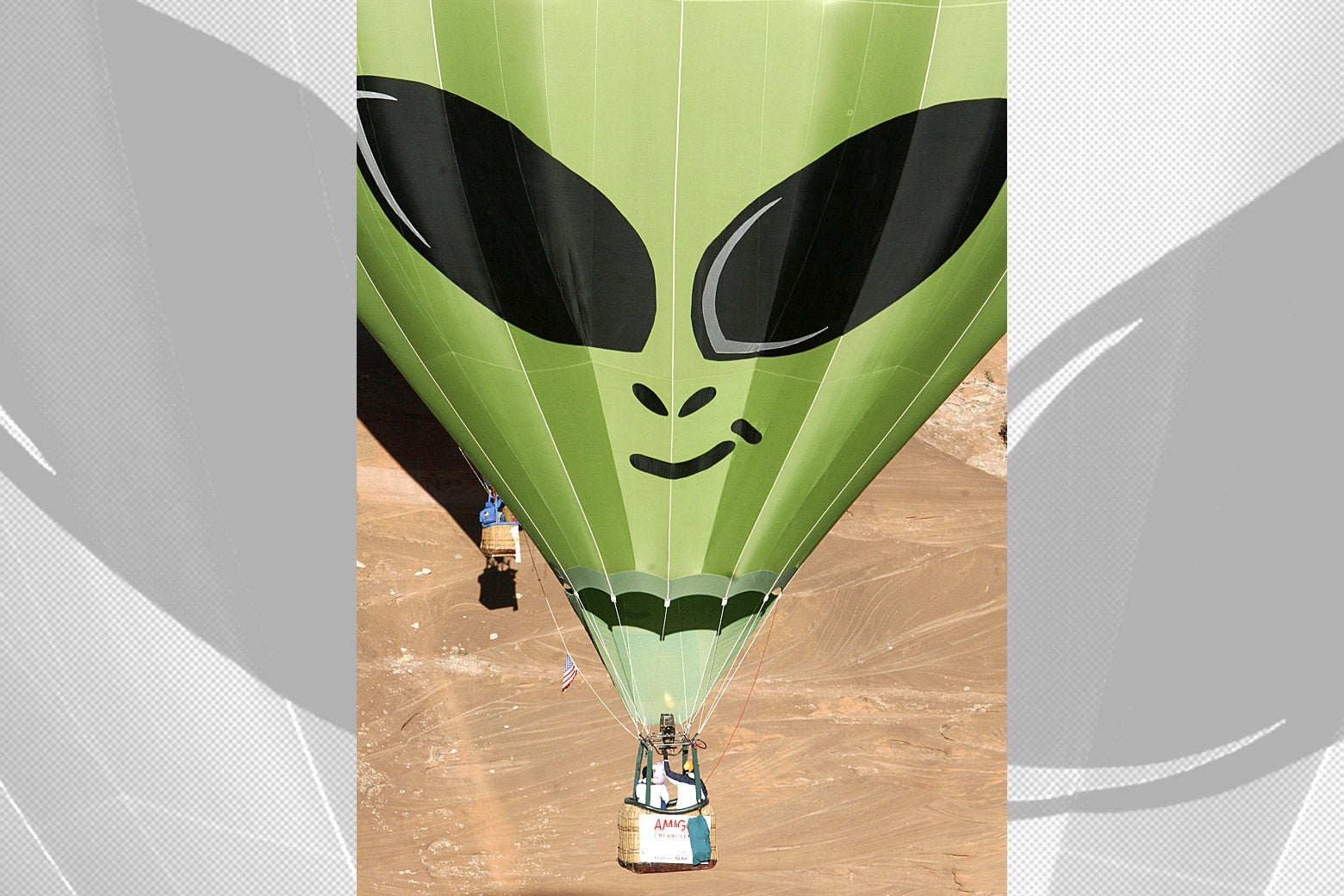 A green hot air ballon with the face of an alien on it.