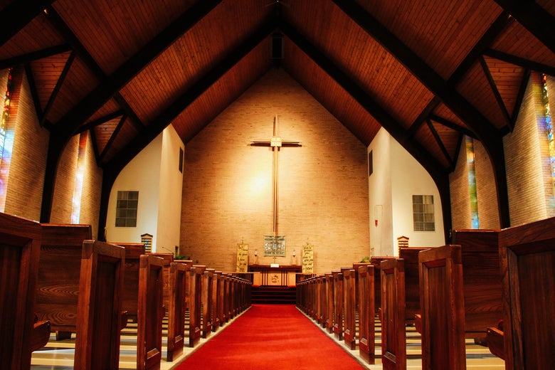 The inside of a church with a cross on the front wall over the altar.