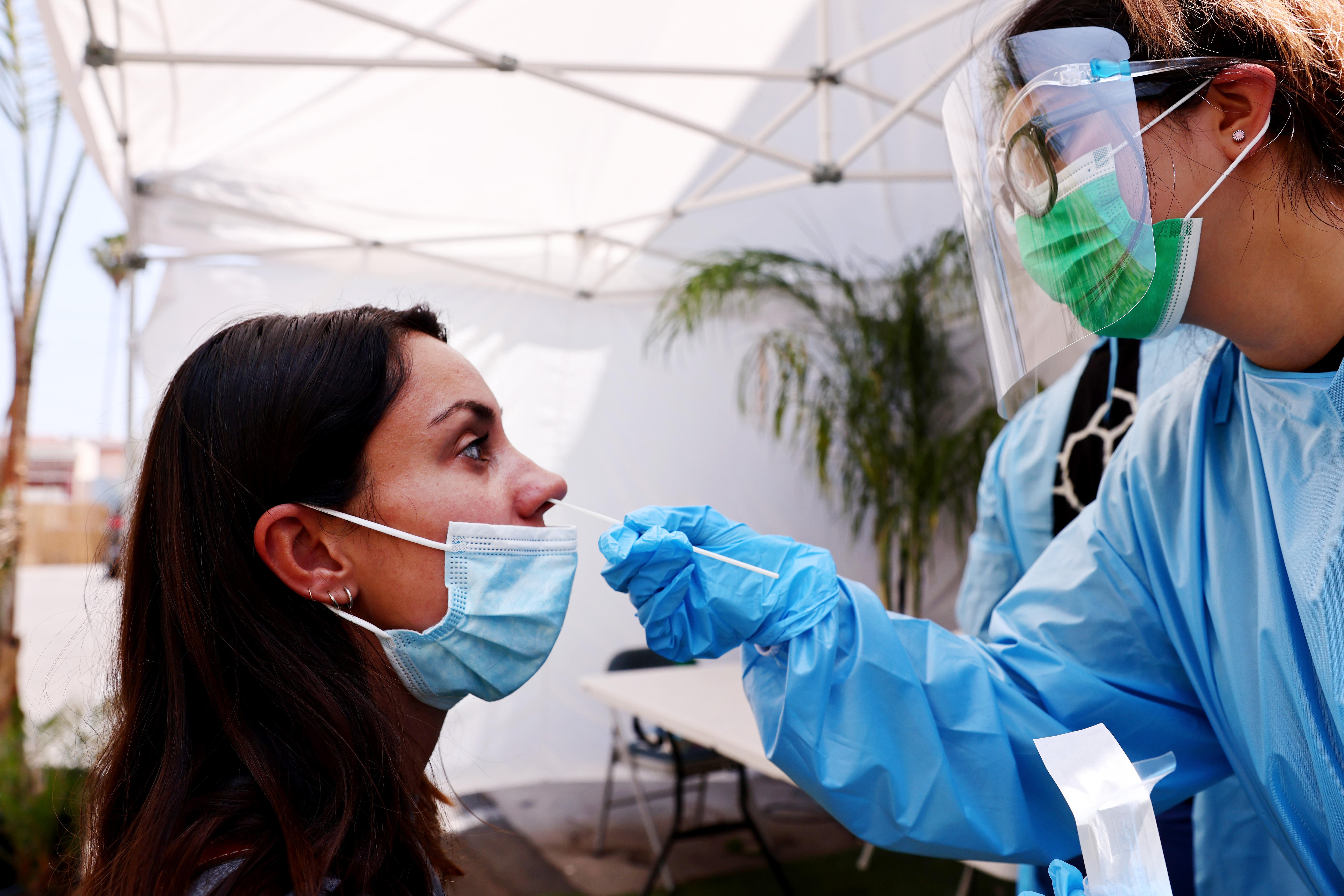 A nurse wearing personal protective equipment inserts a COVID testing swab into a woman's nostril. 
