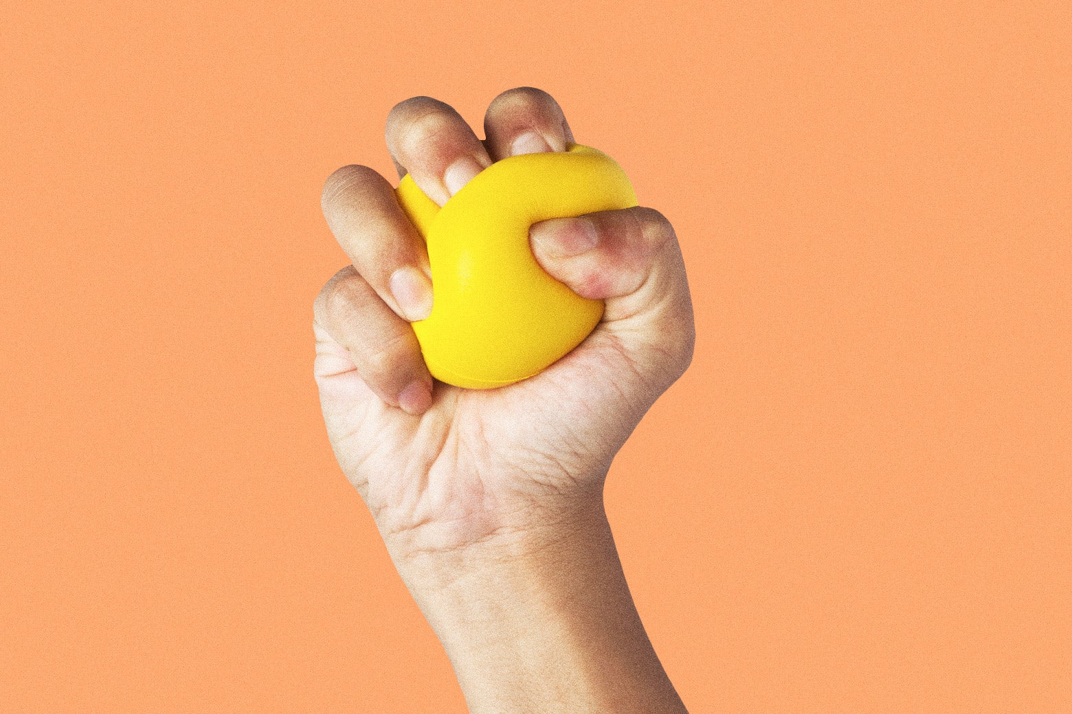 A hand squeezes a yellow stress ball very tightly. 