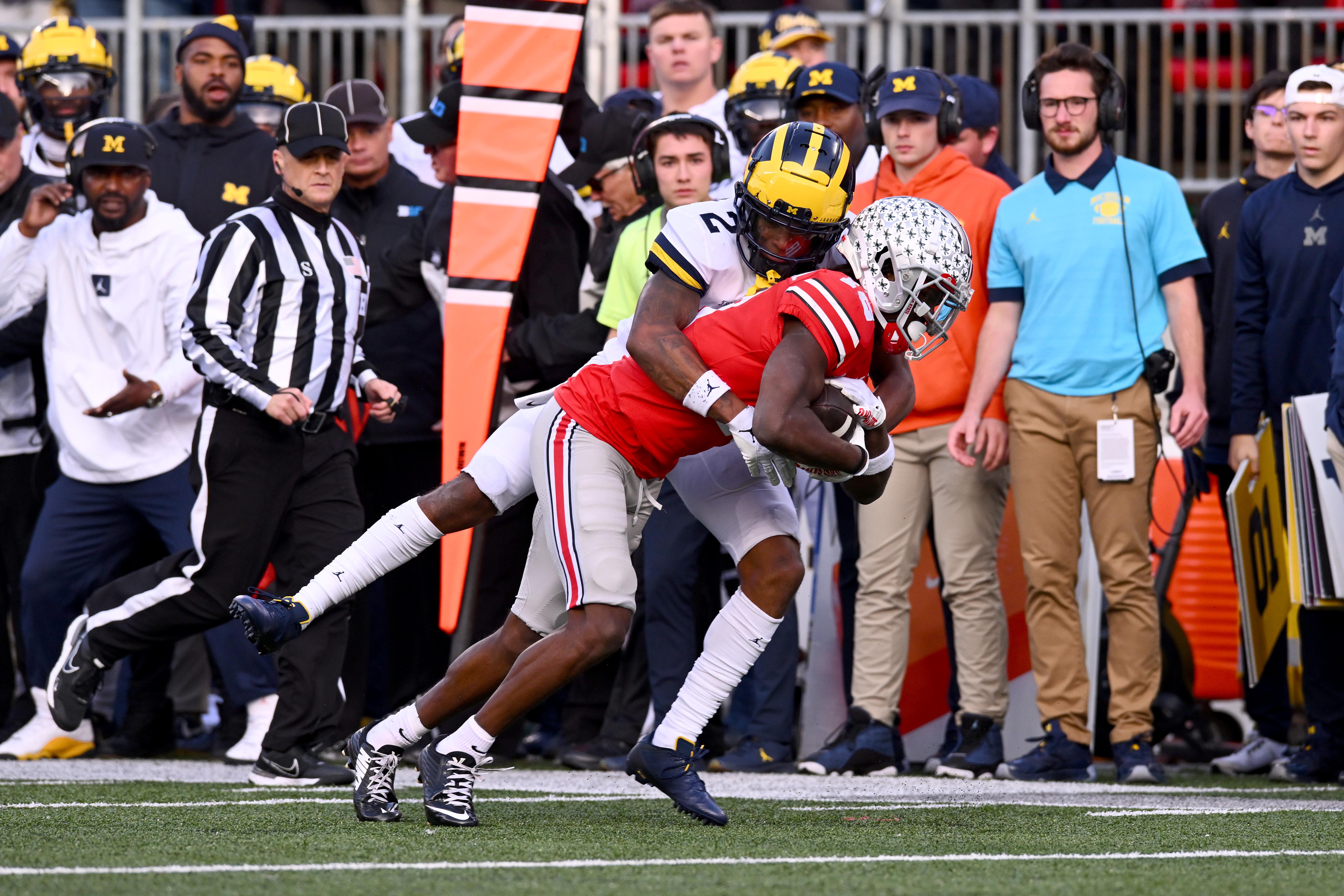 Johnson tackles Harrison Jr., who is carrying the ball, as a ref and Michigan's coaching staff watch on the sidelines