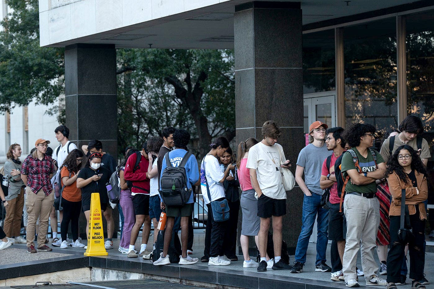 A group of college-age voters stand in line outside a campus building.