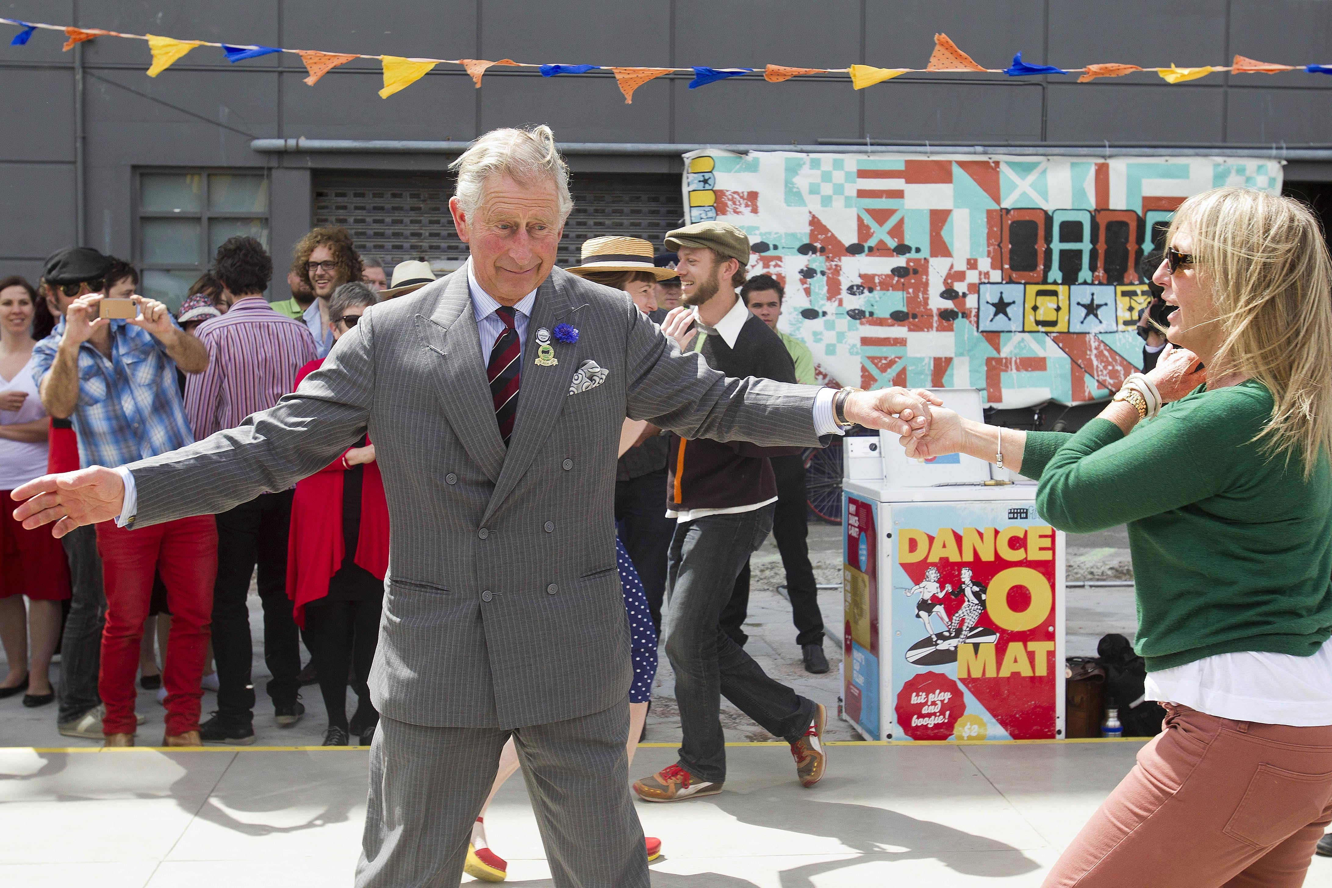 Prince Charles extends his arms while dancing in an empty lot turned civic space in Christchurch, with a crowd behind him
