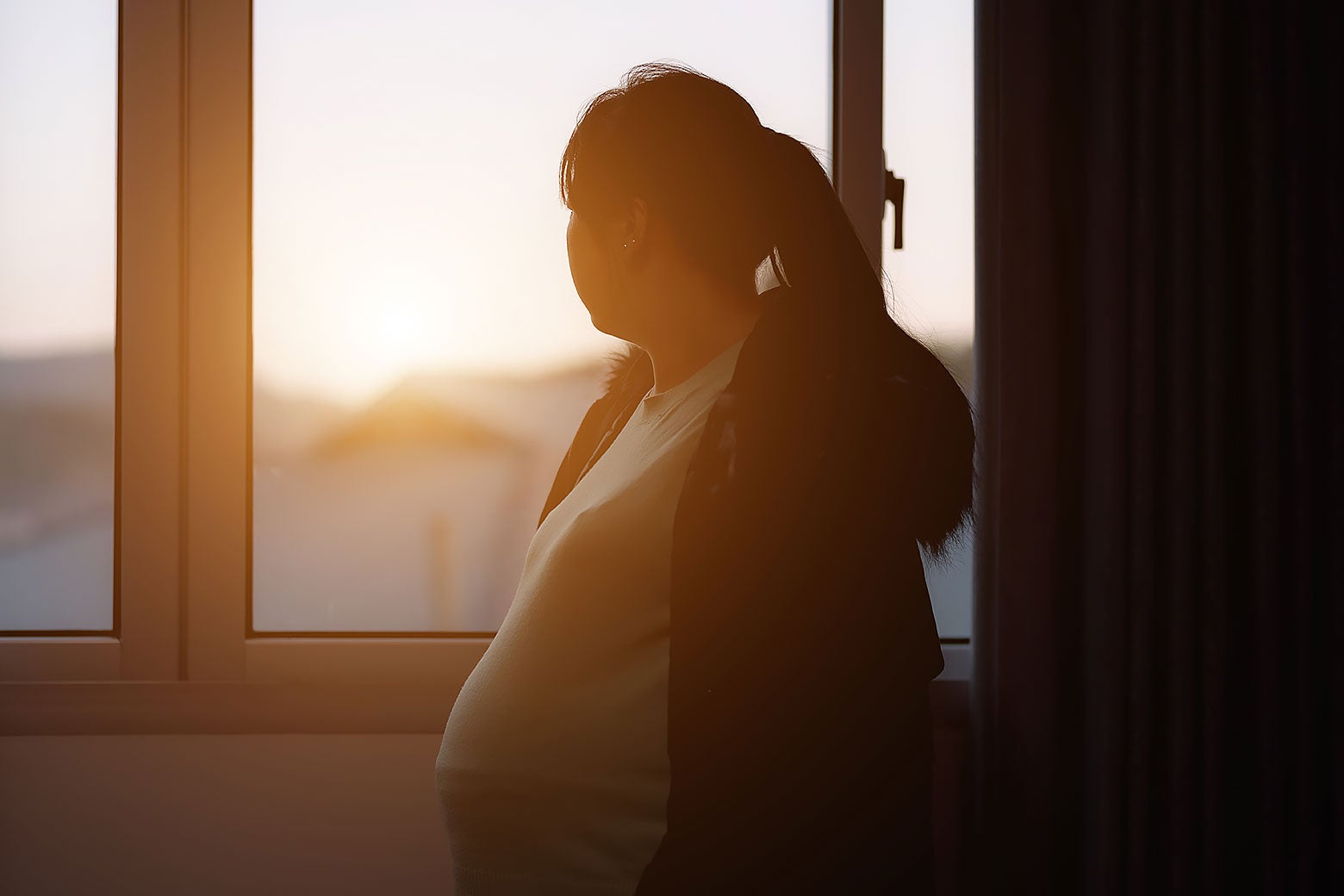 A pregnant woman looking out a window.