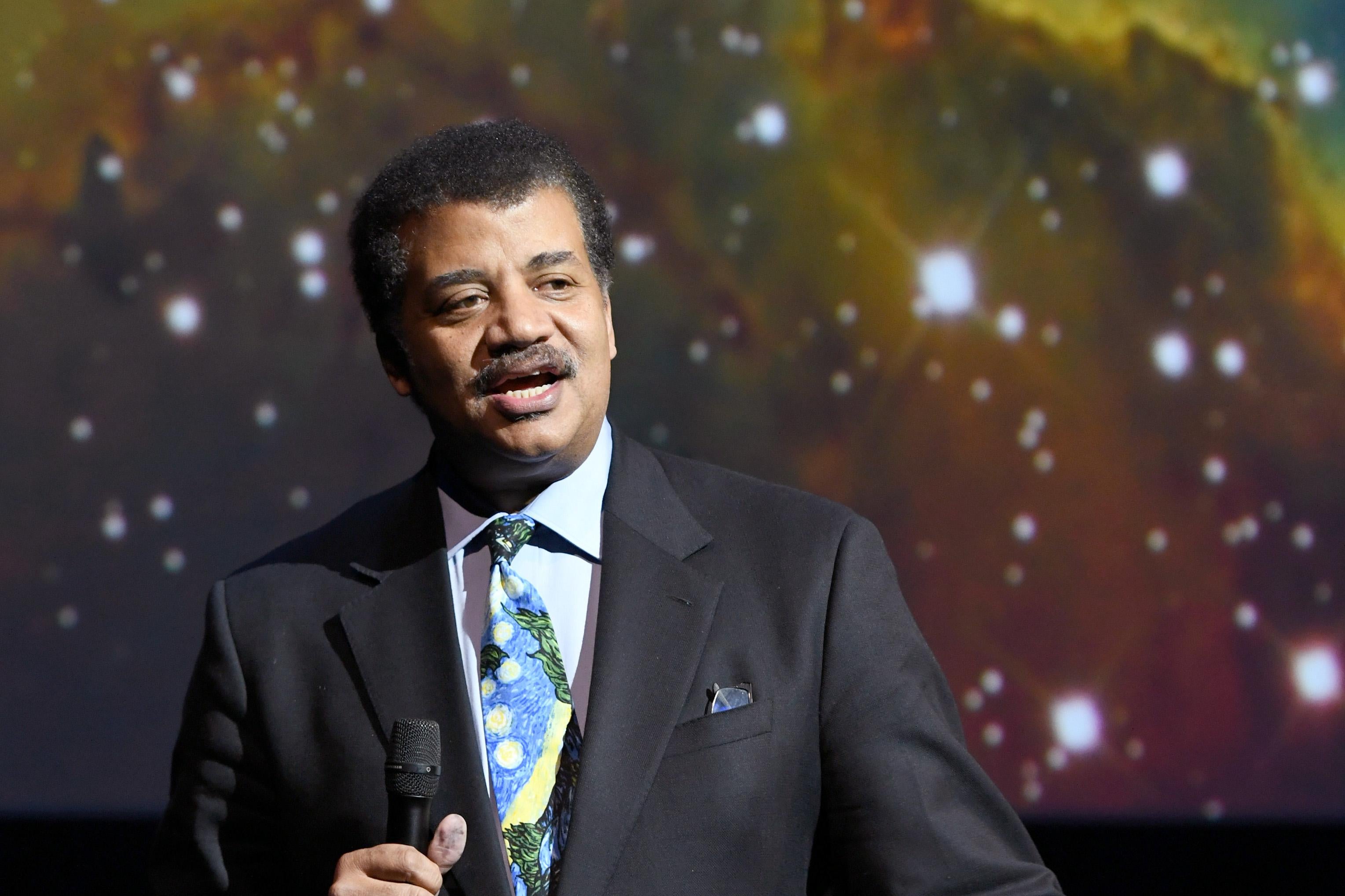 Neil deGrasse Tyson with an image of stars behind him.