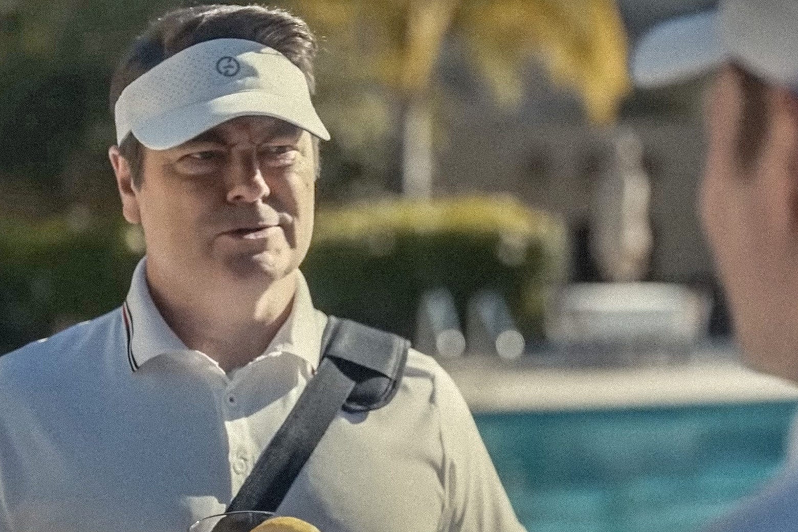 Nick Offerman in a still from the movie wears a visor and a golf polo and looks skeptical. 