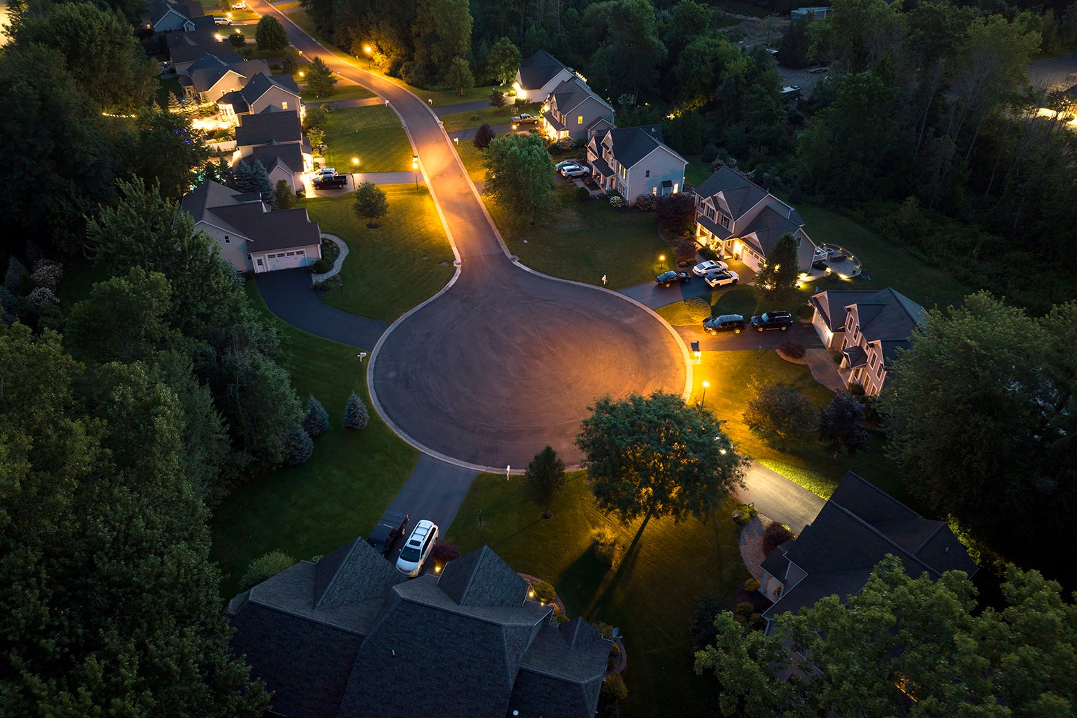 A cul de sac with large single-family homes is seen from above at night and is attractively lit. 