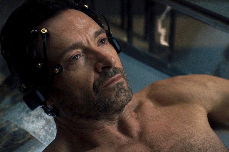 Hugh Jackman, seen shirtless from the shoulders up, lies in a pool of water with nodes attached to his head.