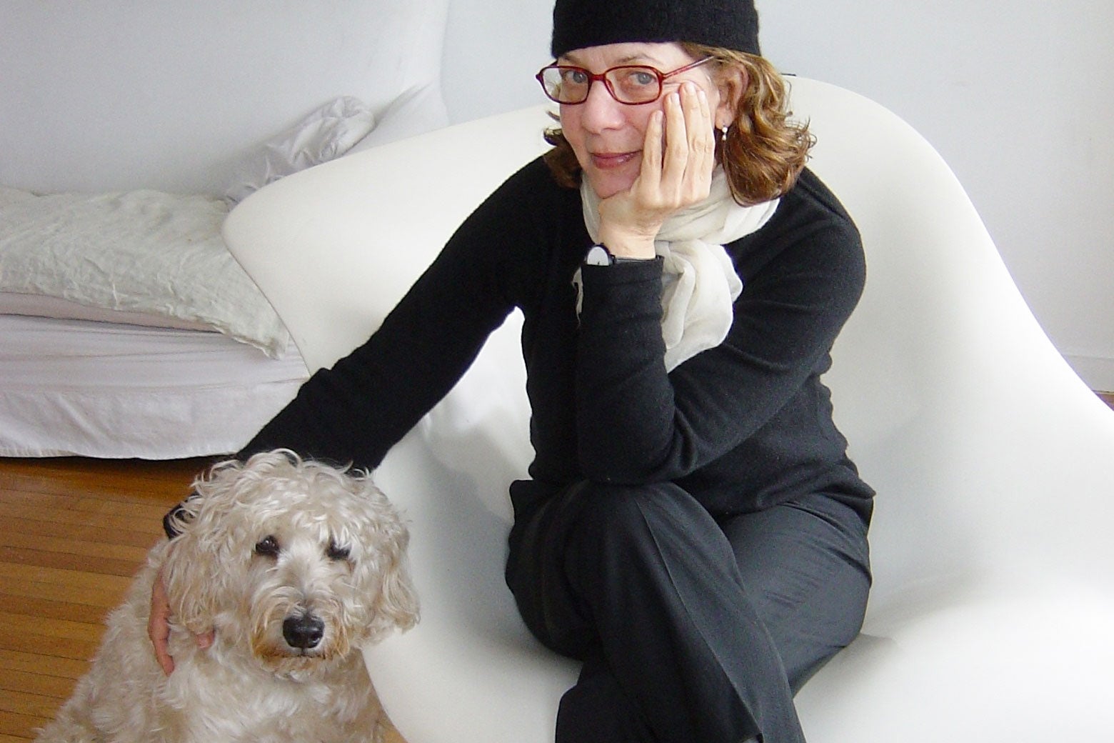 Maira Kalman sits on a white chair and puts her hand on her dog.