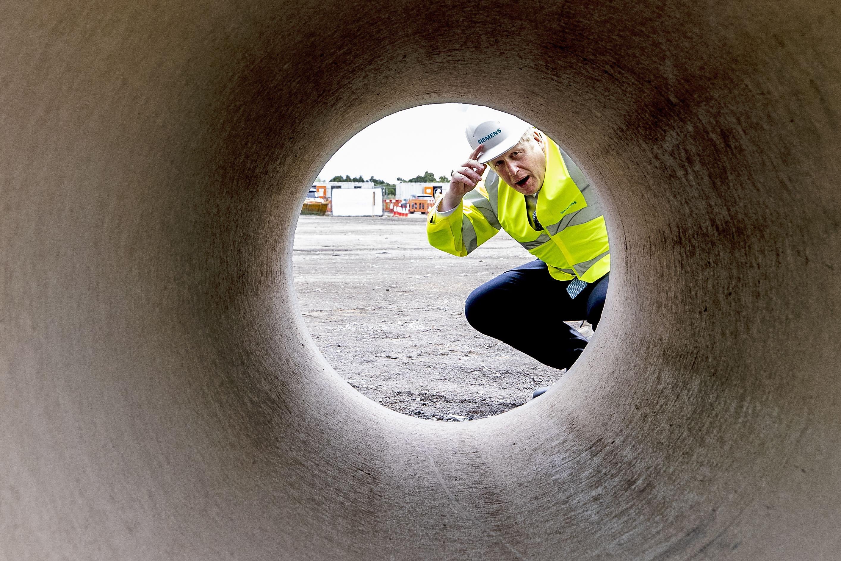 Boris Johnson kneels down to look through a large pipe.