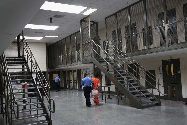 A guard pulls a handcuffed man in an orange jumpsuit.