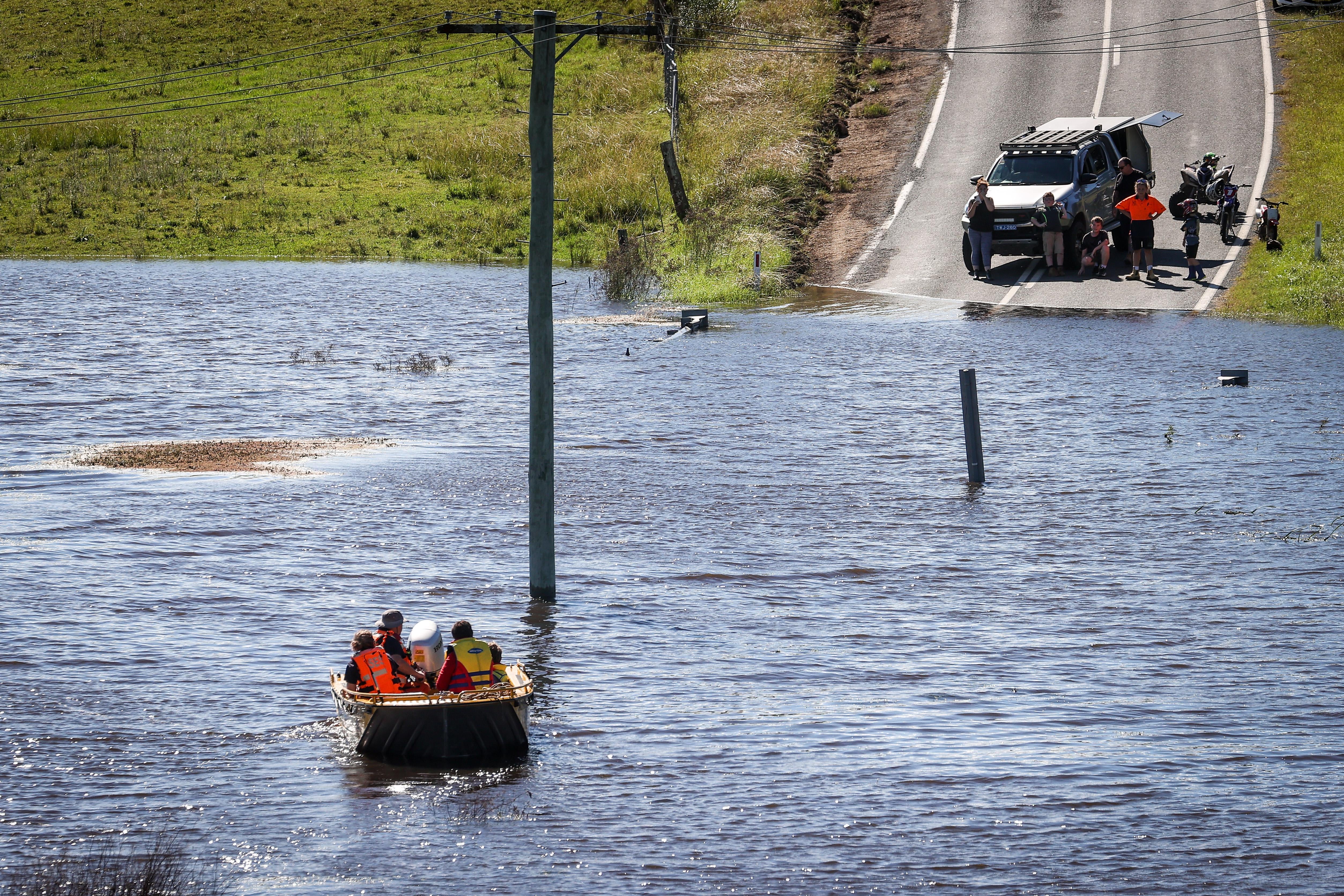 A boat filled with people crosses floodwaters towards a road.