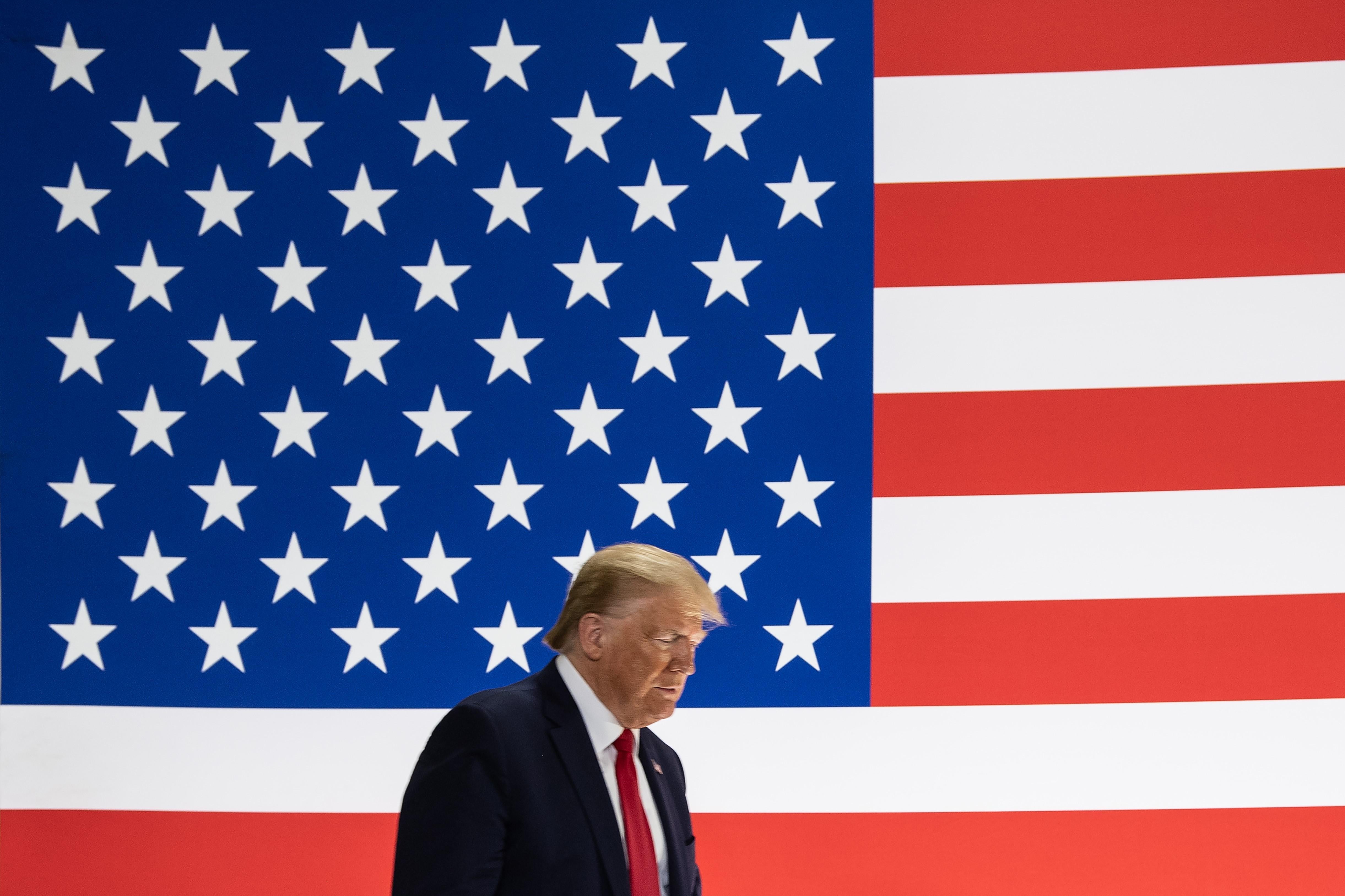 President Donald Trump walks in front of a giant American flag